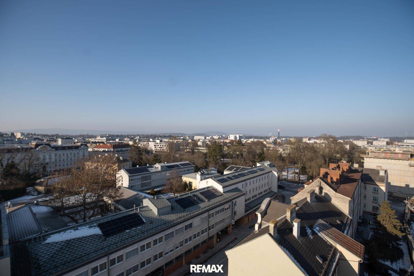 Weitläufiger Panoramablick über die Stadt mit zahlreichen Gebäuden und hügeliger Landschaft im Hintergrund.