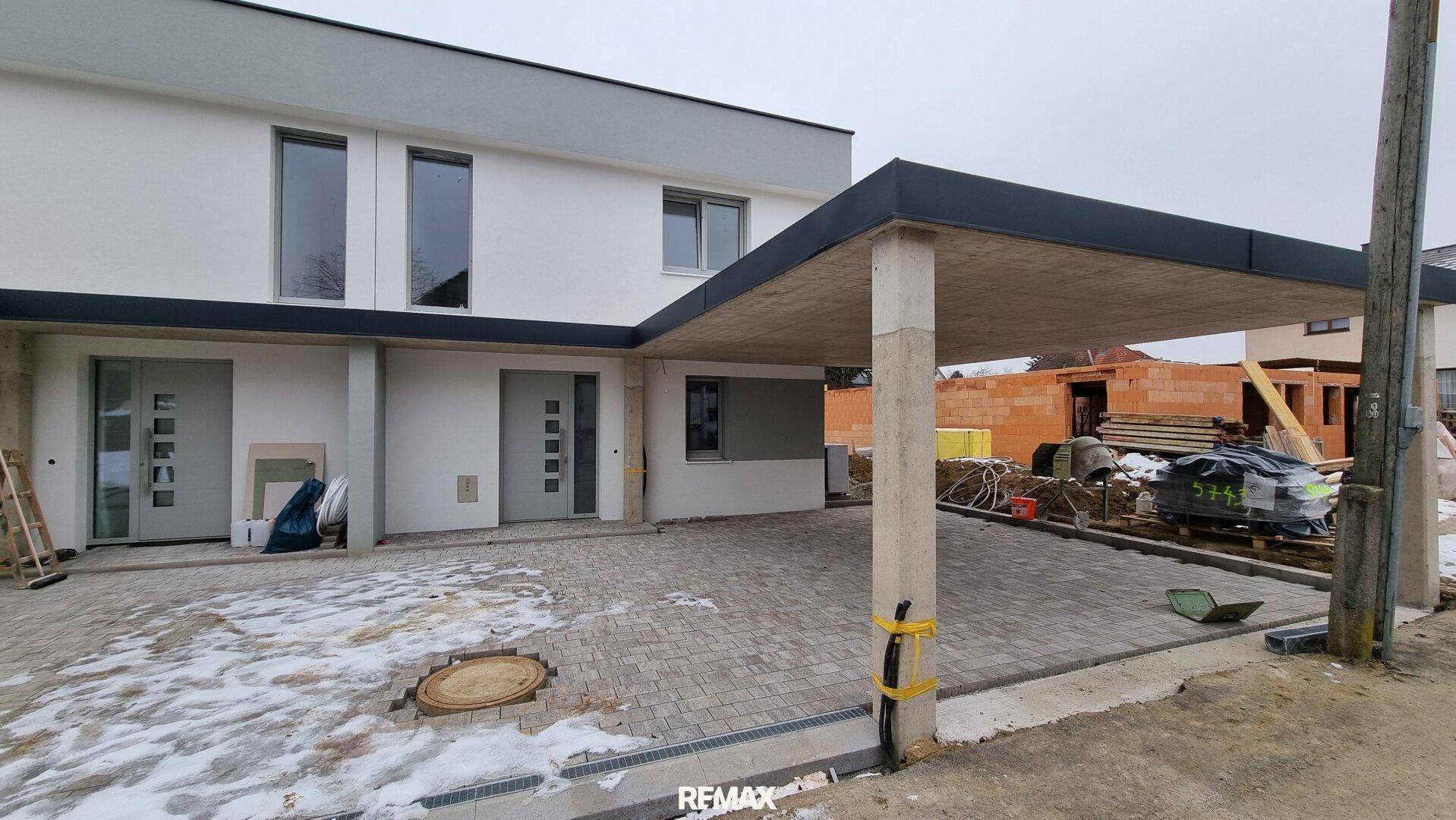 Neubau-Doppelhaushälfte mit Carport und Baustelle im Vordergrund.
