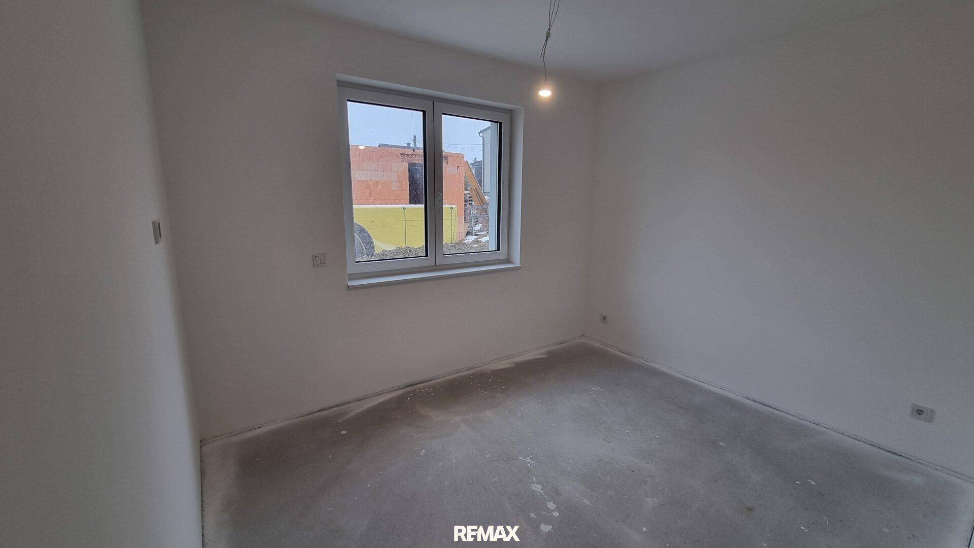 Leeres Schlafzimmer im Rohbauzustand mit einem Fenster und viel Tageslicht.