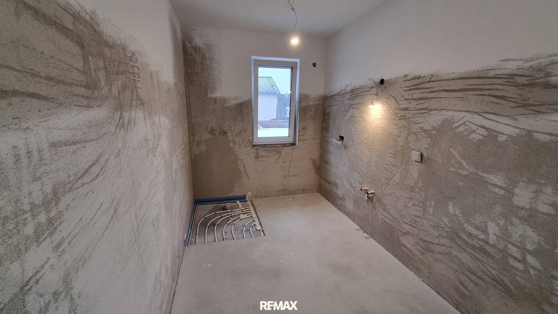 Unfertiges Badezimmer mit vorbereiteten Anschlüssen für eine Dusche und Fenster.