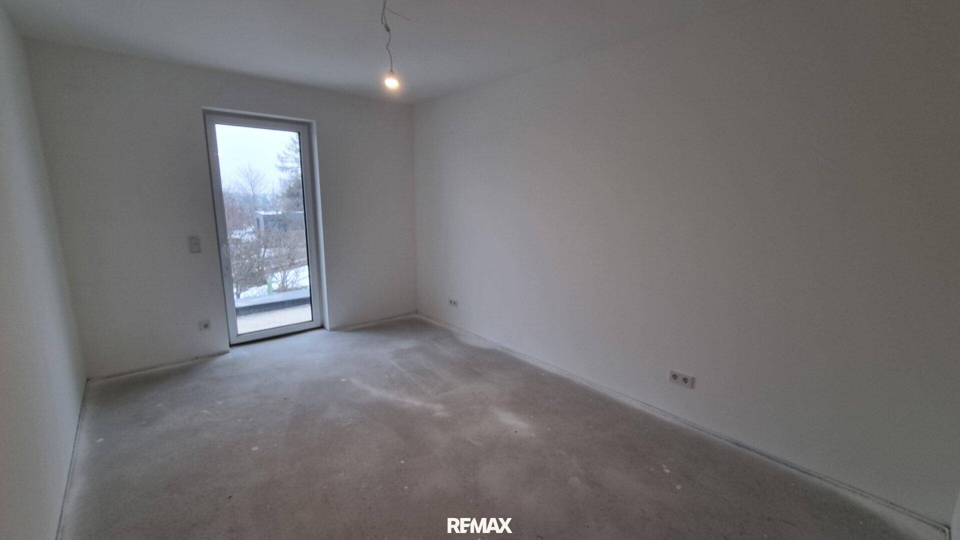 Helles Zimmer mit Zugang zu einem zukünftigen Balkon oder einer Terrasse und unfertigem Boden.