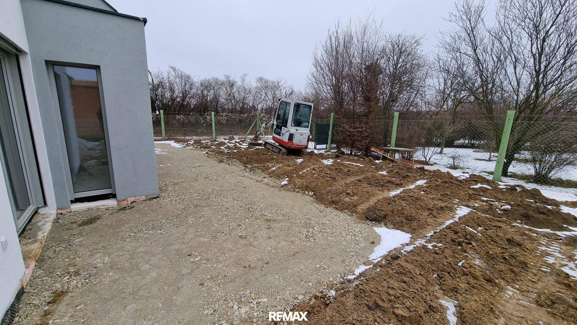 Außenansicht des Neubaus mit Baustelle, Bagger und unfertigem Gartenbereich im Winter.