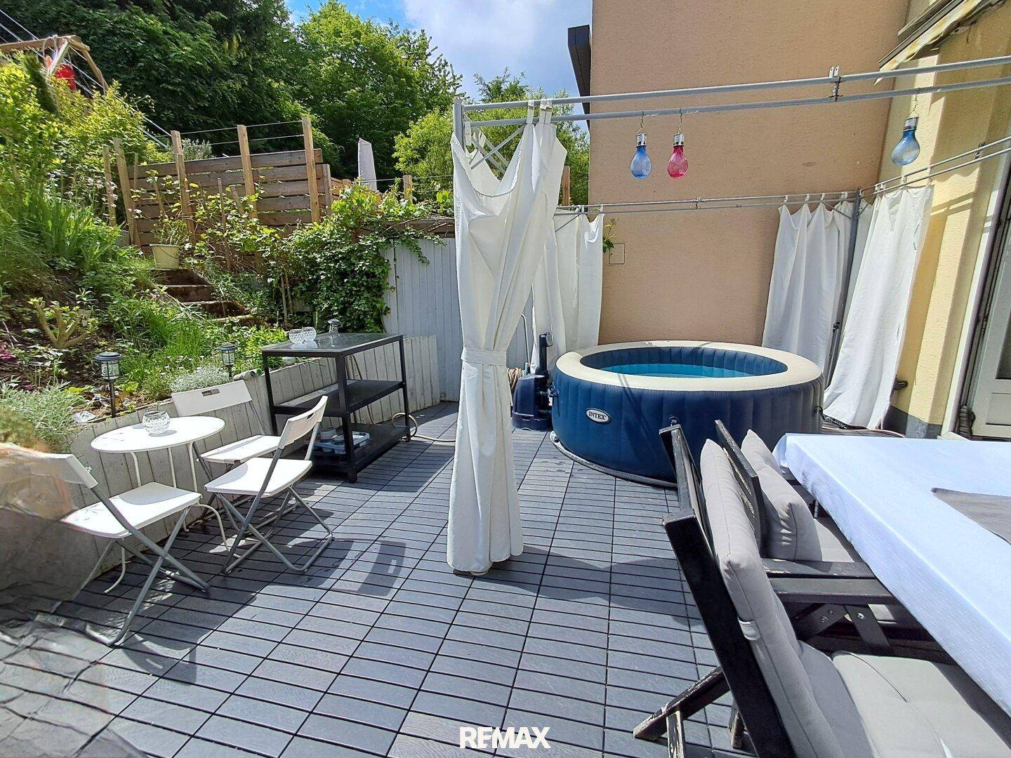 Geräumige Terrasse mit Essbereich, Whirlpool und Blick auf den grünen Gartenbereich.