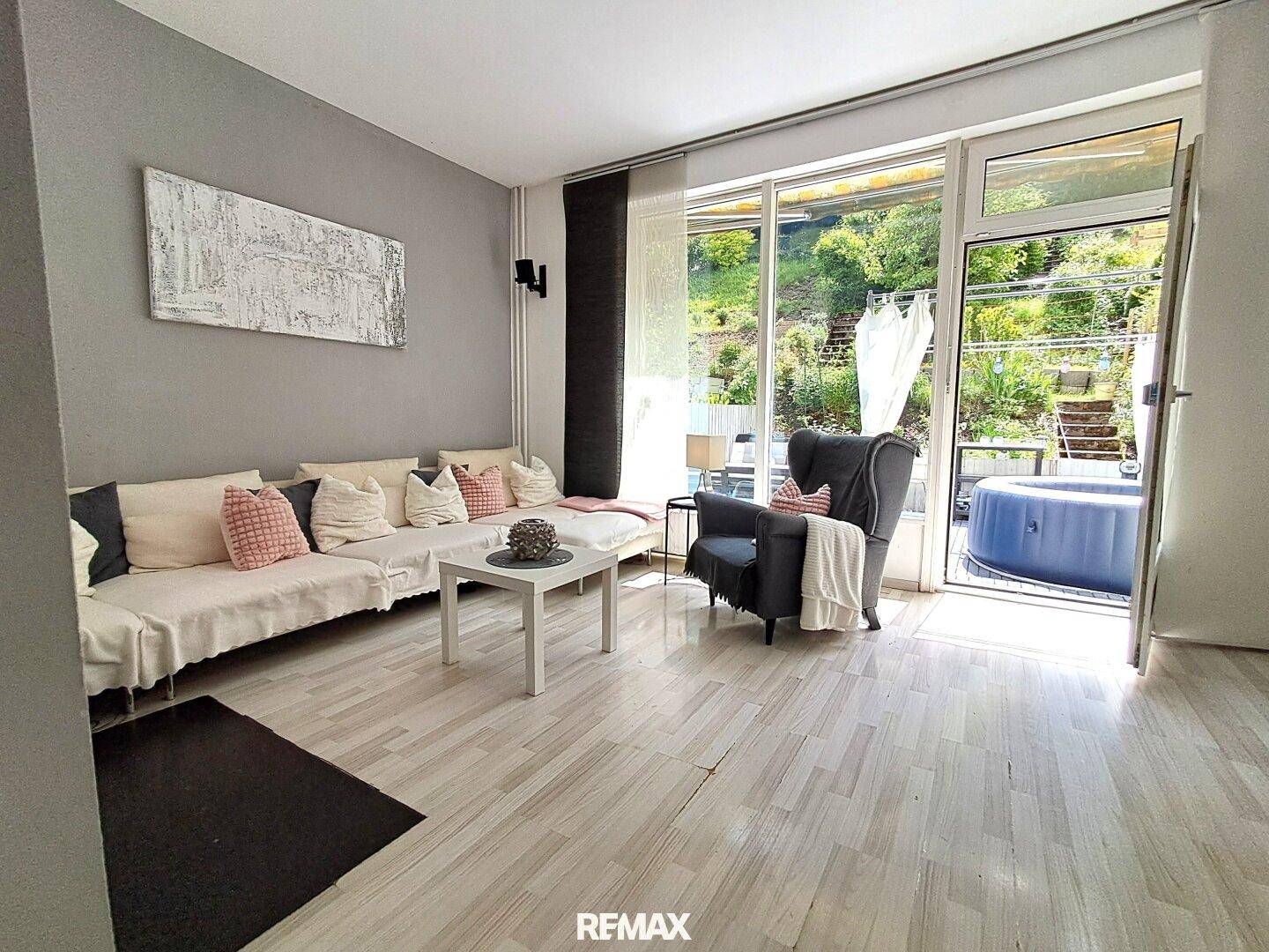 Helles Wohnzimmer mit hellem Laminatboden, bequemer Couch und Zugang zur Terrasse mit Whirlpool.
