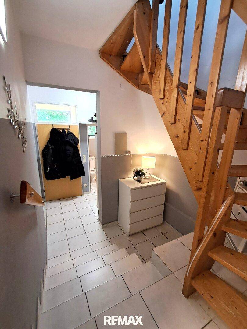 Heller Eingangsbereich mit Holztreppe und Fliesenboden, der zu den oberen Etagen führt.