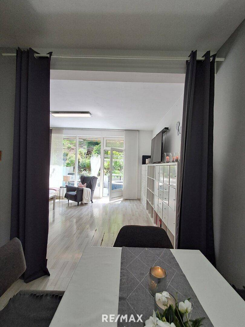 Offener Wohnbereich mit Blick auf die Terrasse und den Garten, getrennt durch Vorhänge.