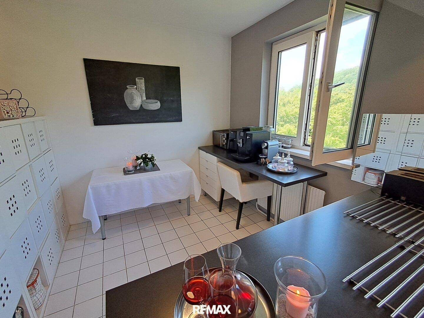 Funktionale Küche mit weißen Schränken, dunkler Arbeitsplatte und Essbereich am Fenster.