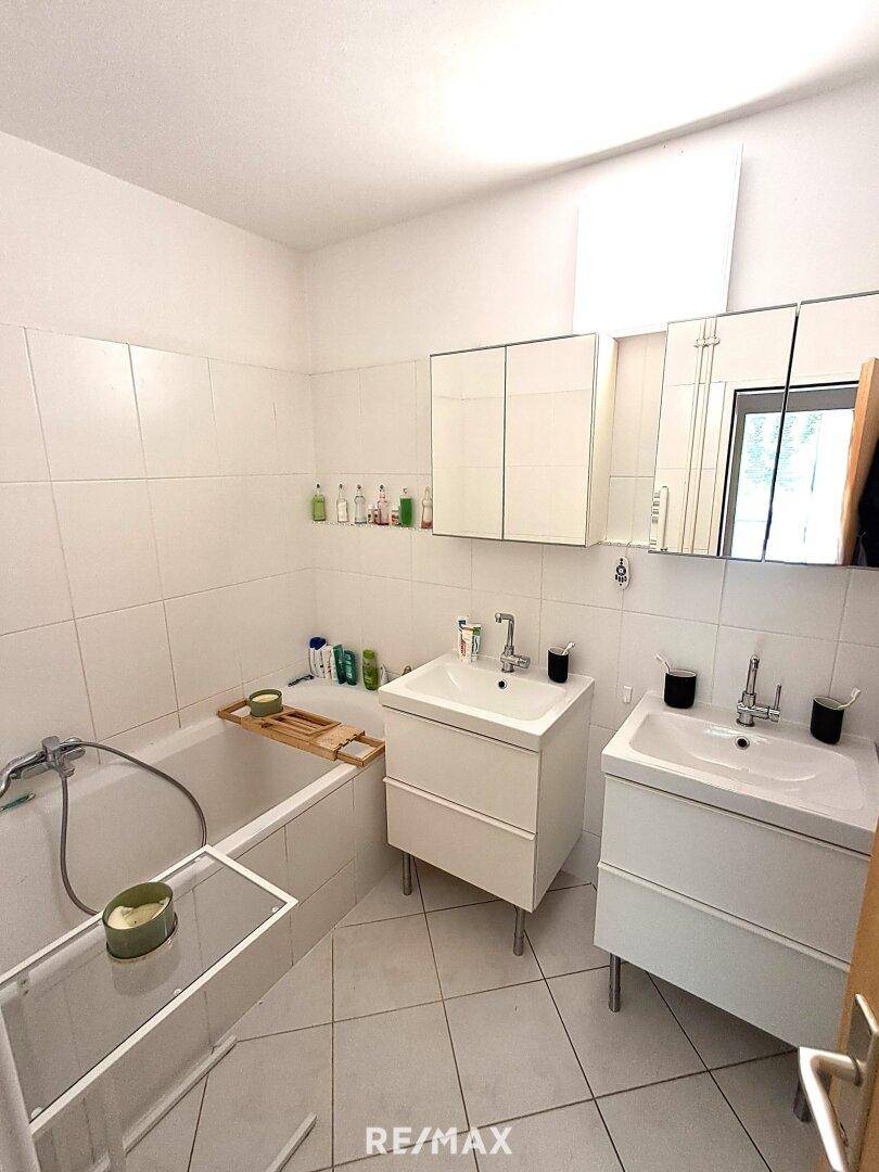 Badezimmer mit Badewanne, Doppelwaschbecken und weißen Fliesen.