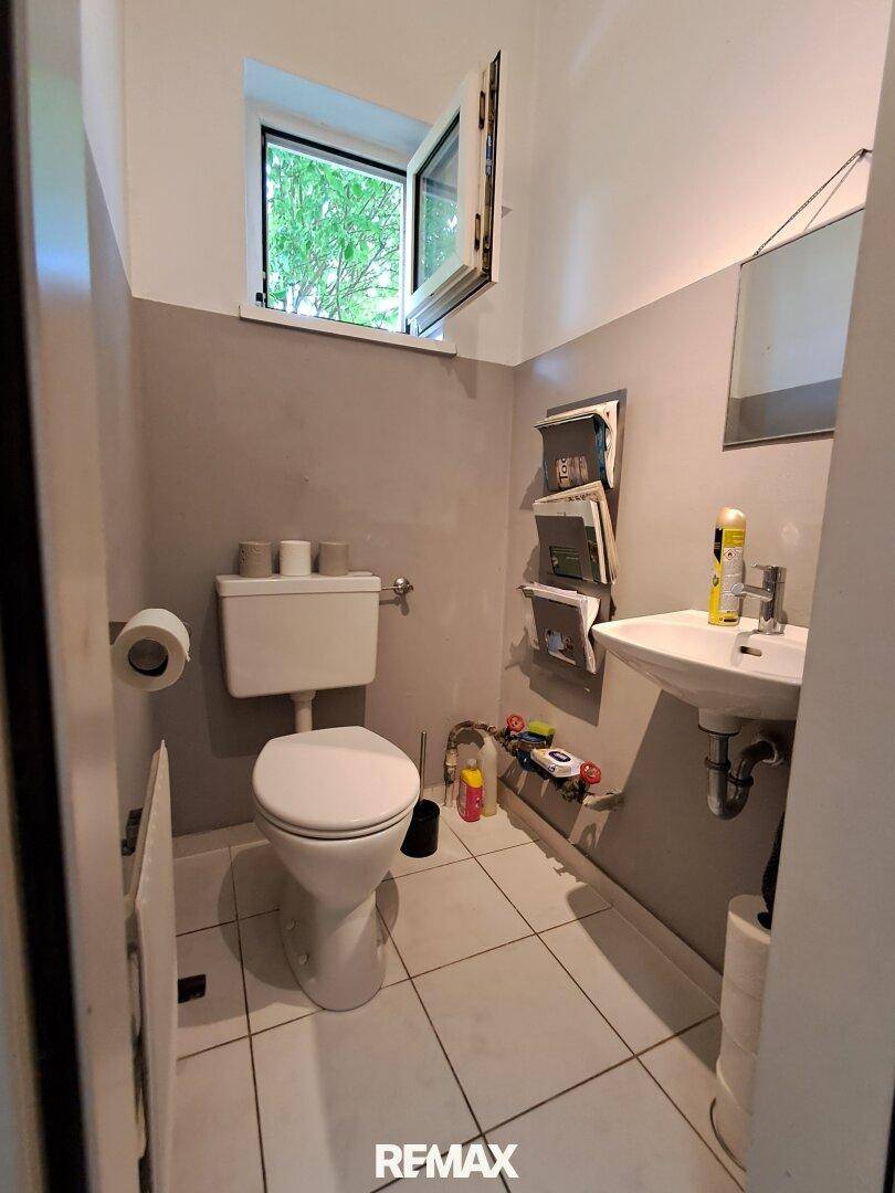 Kleines Gäste-WC mit Fenster, Toilette und Waschbecken, ausgestattet mit weißen Fliesen.