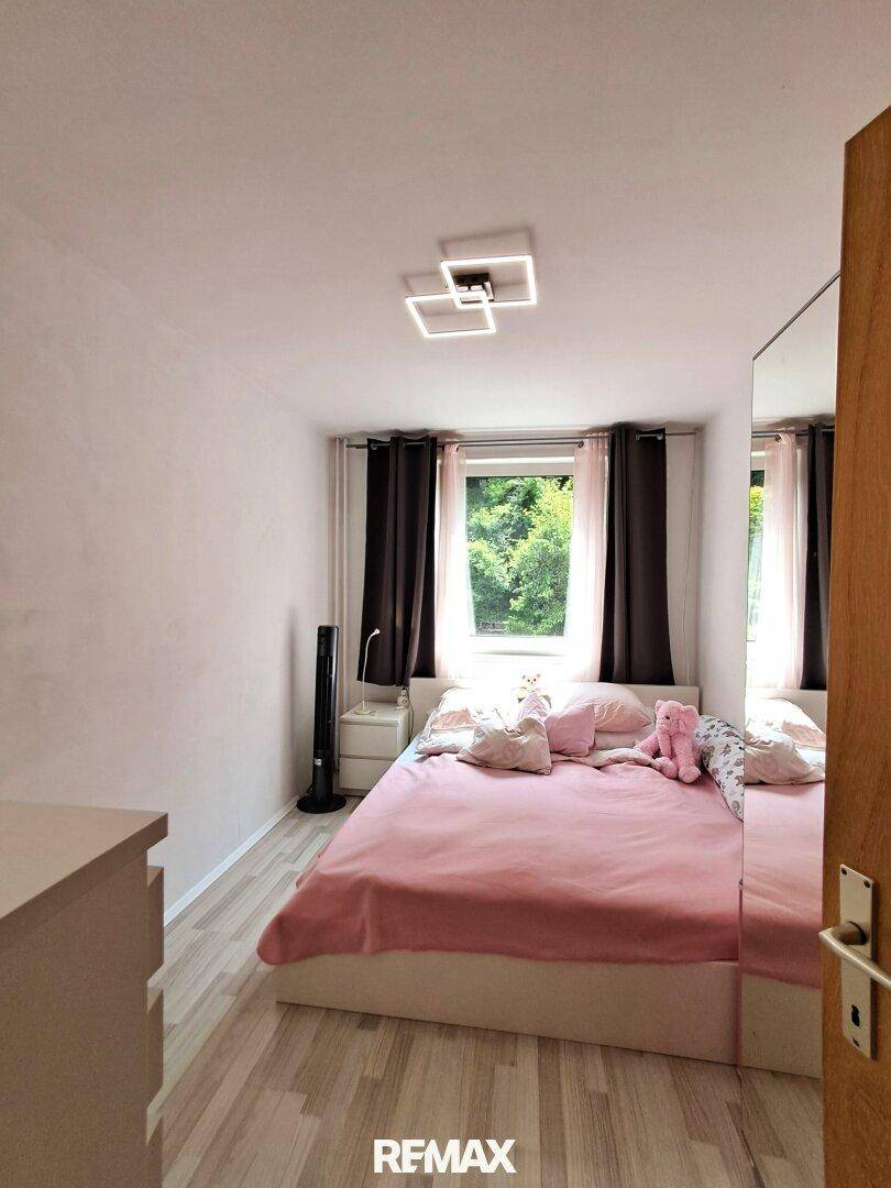 Helles Kinderzimmer mit rosa Bettwäsche, Laminatboden und Fenster mit Blick nach draußen.