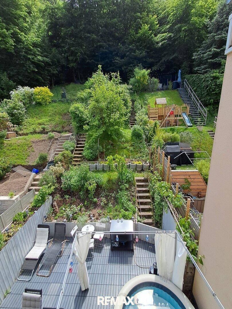 Weitläufiger Gartenbereich am Hang mit Terrasse, Whirlpool und Spielplatz im Hintergrund.