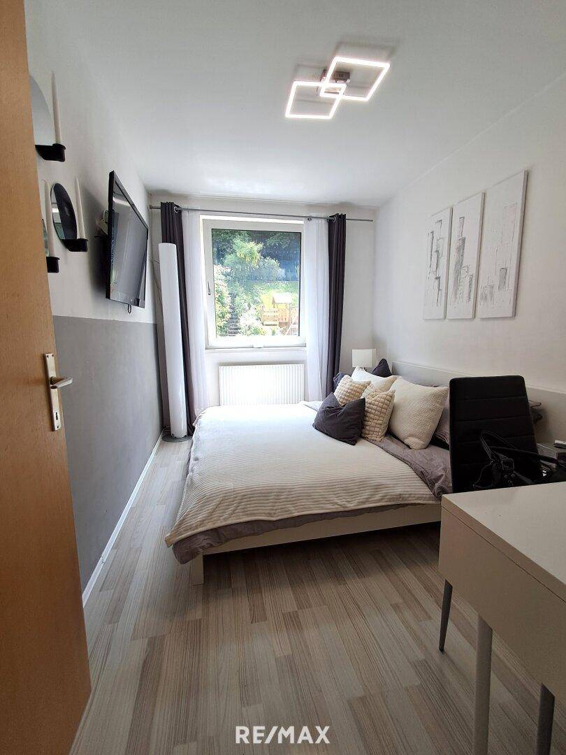 Schlafzimmer mit hellem Laminatboden, großem Fenster und Blick ins Grüne.