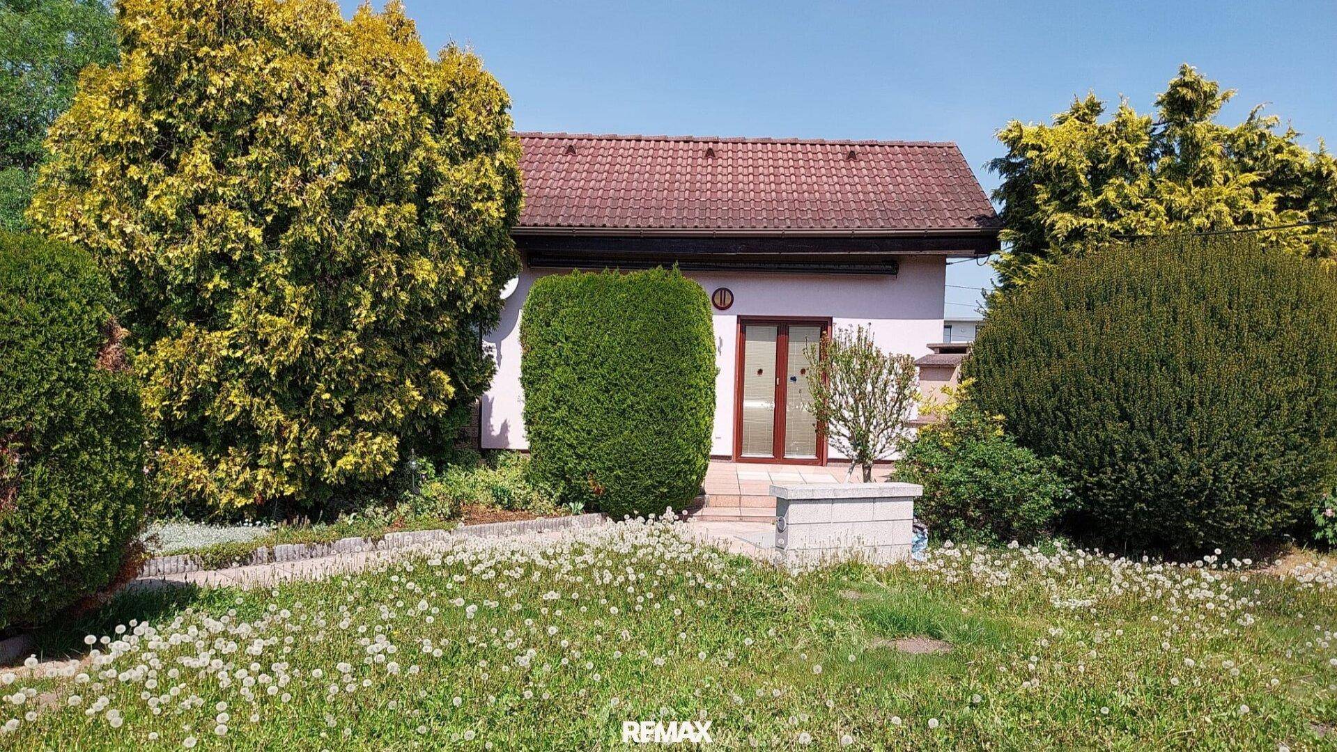 Einfamilienhaus mit gepflegtem Vorgarten, umgeben von hohen Hecken und Bäumen.