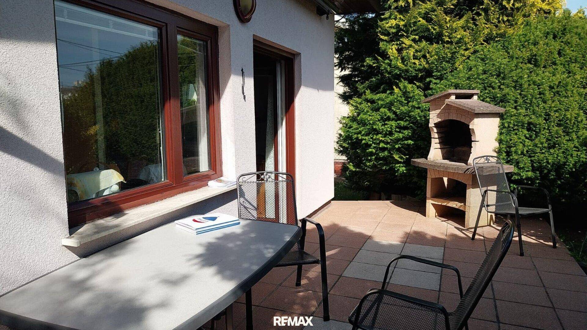 Sonnige Terrasse mit Gartenmöbeln und gemauertem Grill für gesellige Stunden.