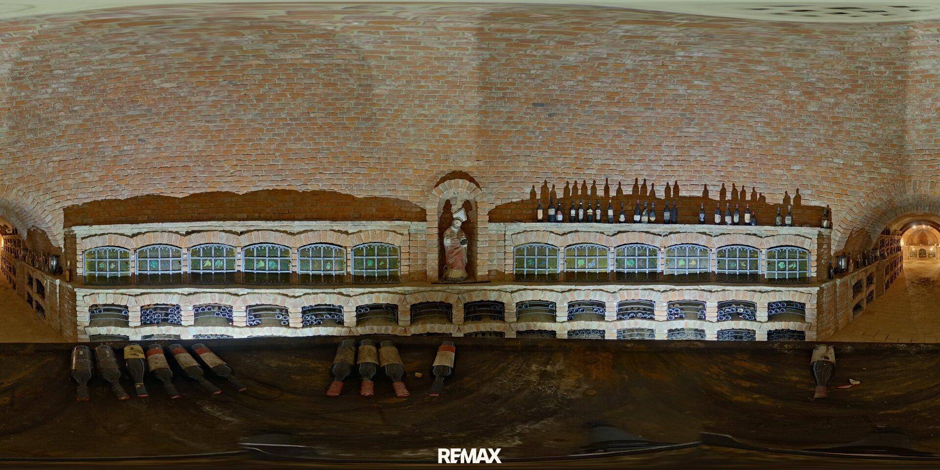 Panoramablick auf eine lange Wand im Weinkeller mit Ziegeln, Nischen und Weinflaschen.