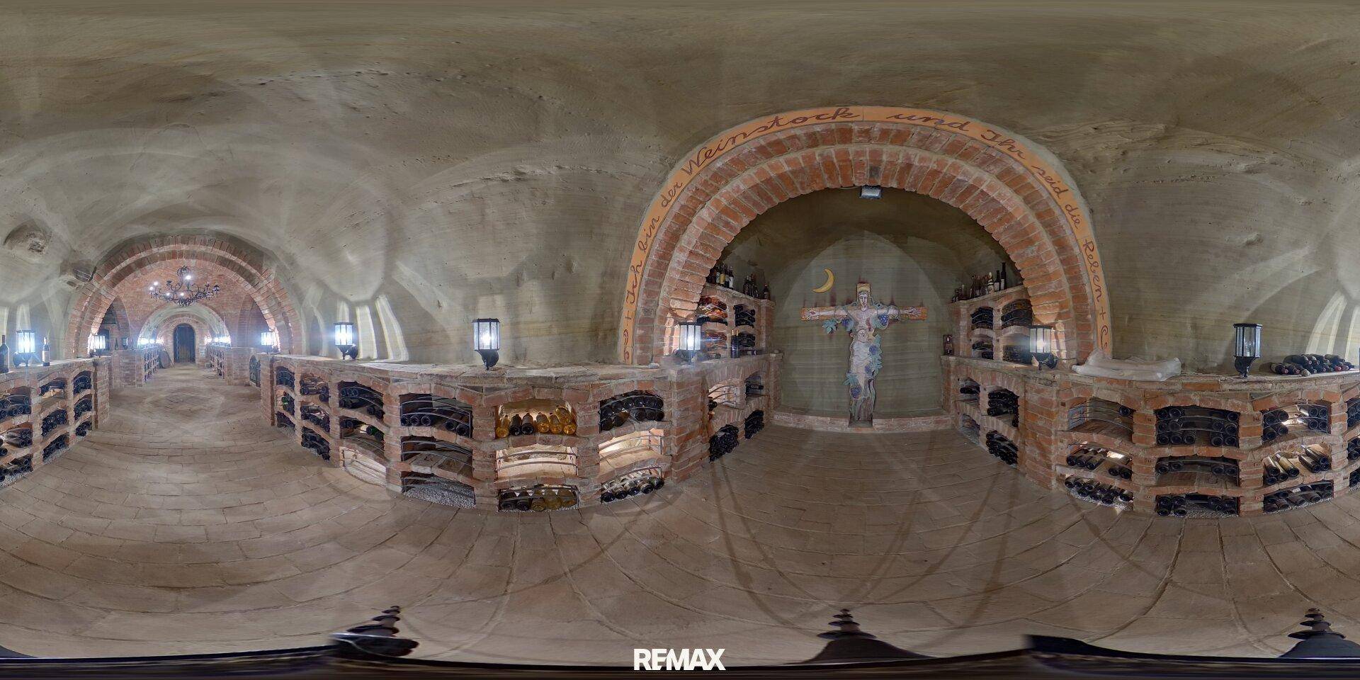 Panoramablick in einen Weinkeller mit Ziegelgewölbe, Weinregalen und einer zentralen Skulptur.