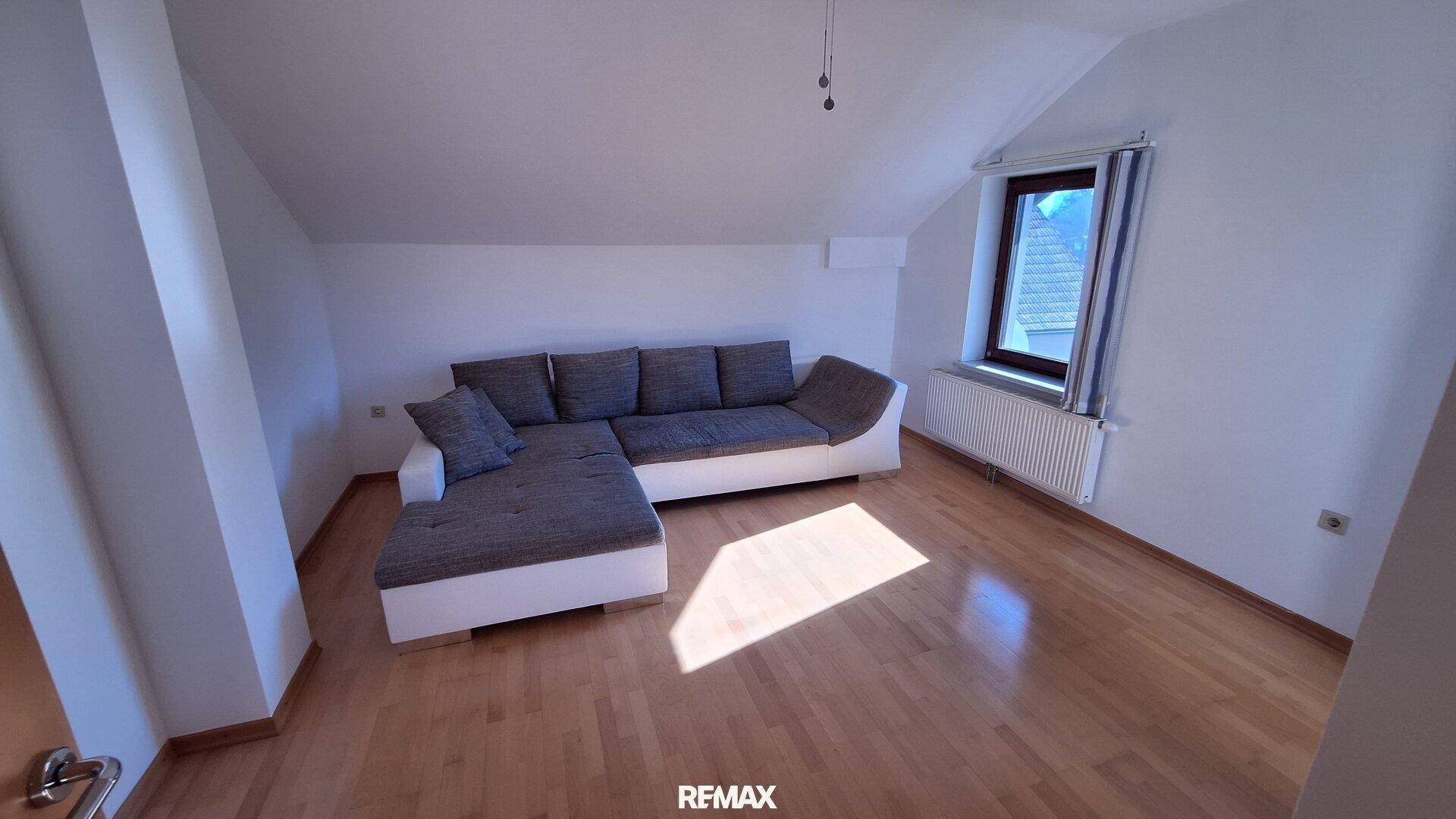 Helles Wohnzimmer im Dachgeschoss mit gemütlichem Sofa, Holzboden und Dachschräge.