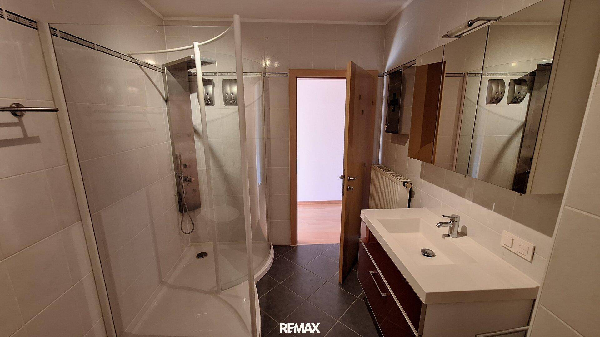 Modernes Badezimmer mit Duschkabine, Einzelwaschbecken und dunklen Bodenfliesen.