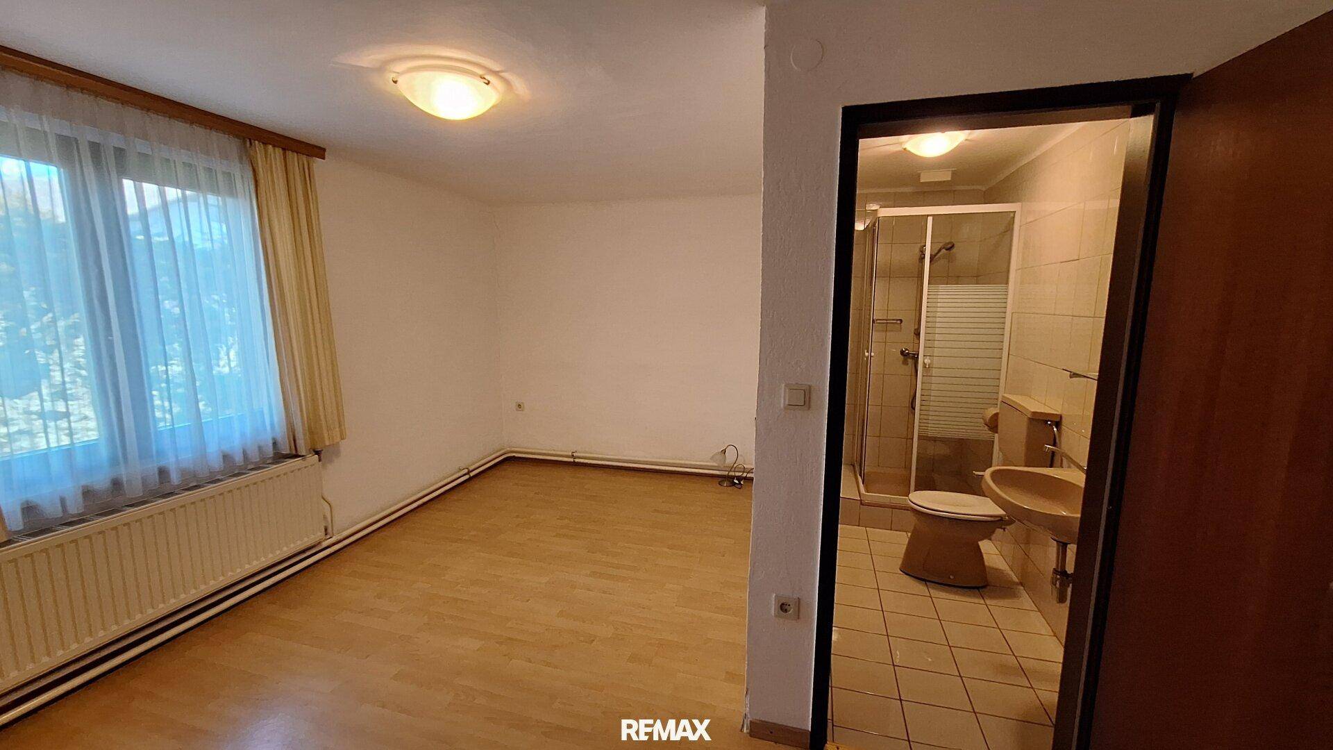 Helles Schlafzimmer mit Parkettboden und angrenzendem Badezimmer mit Dusche.