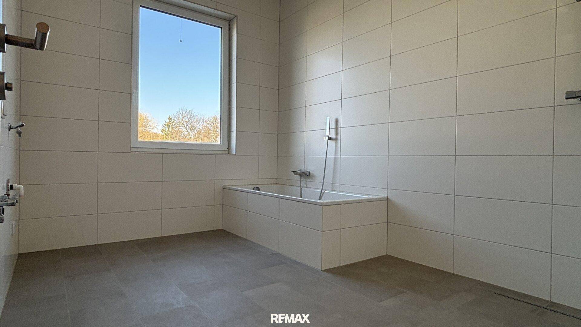 Modernes Badezimmer mit großer Badewanne, hellen Fliesen und Fenster für Tageslicht.