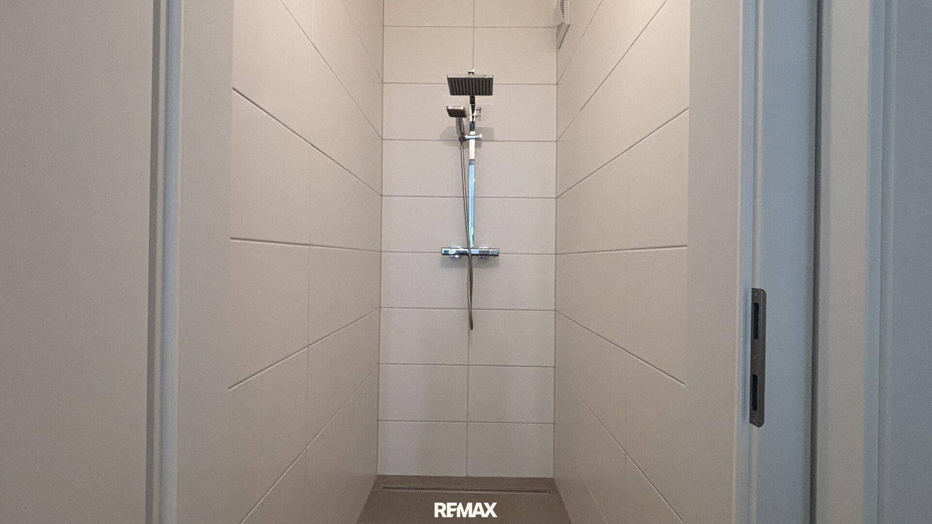 Moderne begehbare Dusche mit Regenduschkopf und hellen Wandfliesen.