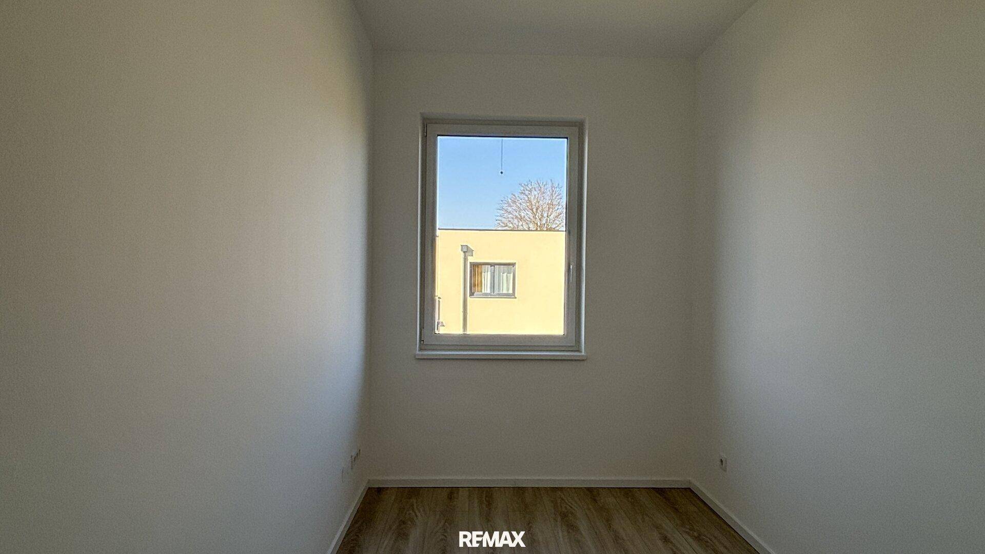 Helles Schlafzimmer mit Laminatboden und einem Fenster mit Blick ins Grüne.