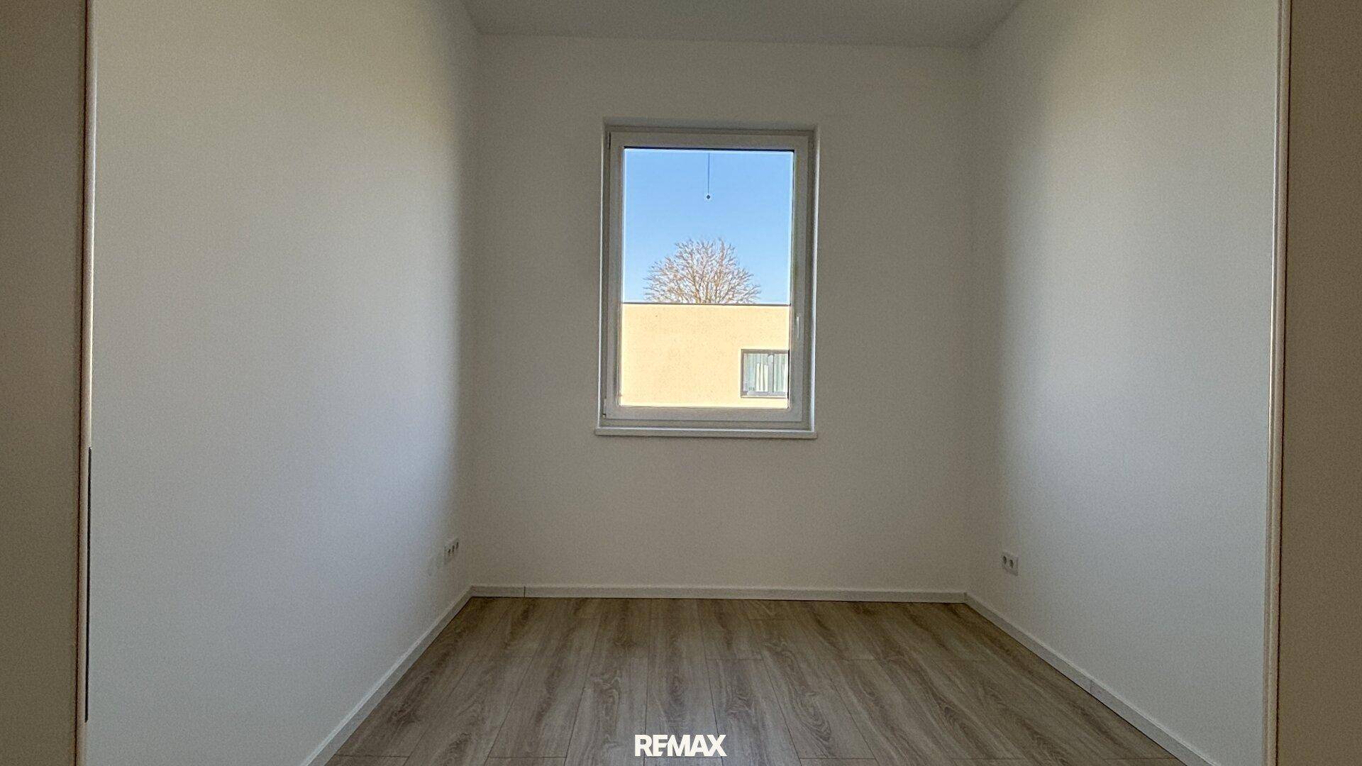 Geräumiges Schlafzimmer mit hellem Laminatboden und viel Tageslicht durch das Fenster.
