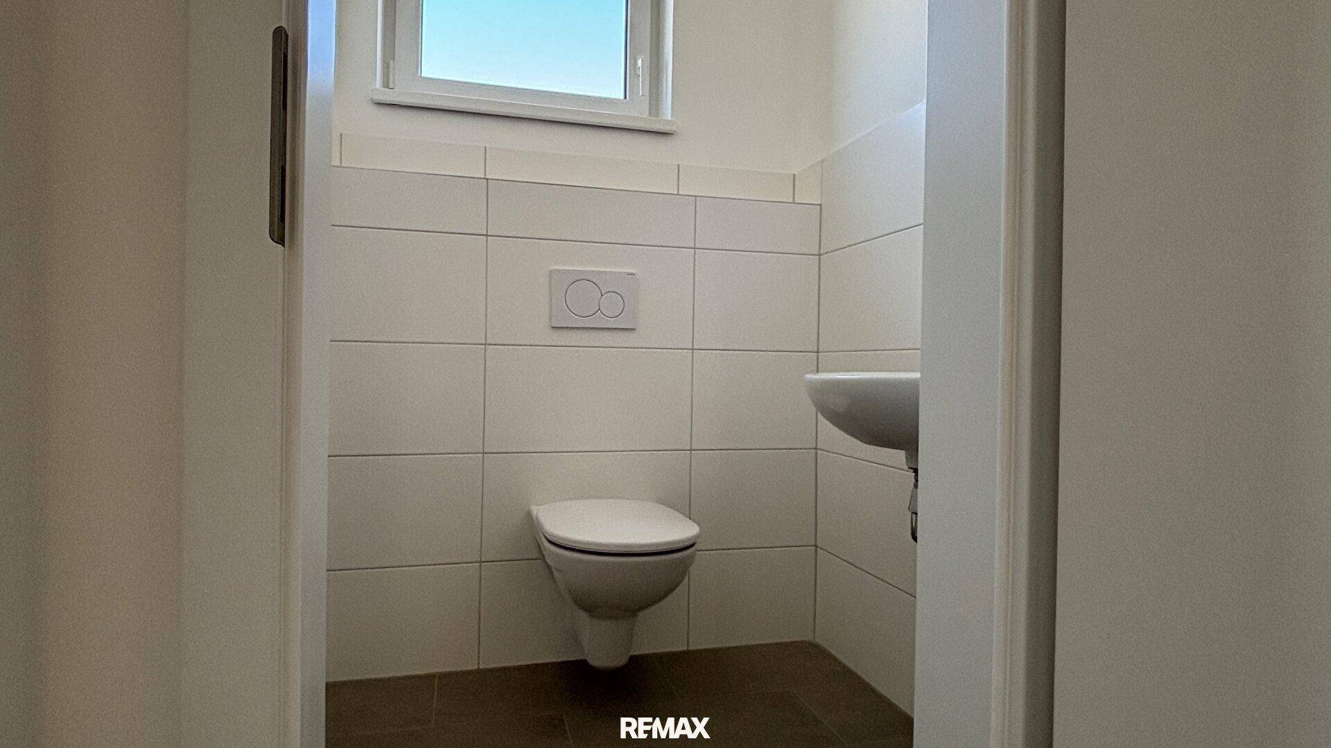 Kleines Gäste-WC mit wandhängendem WC, Waschbecken und Fenster.