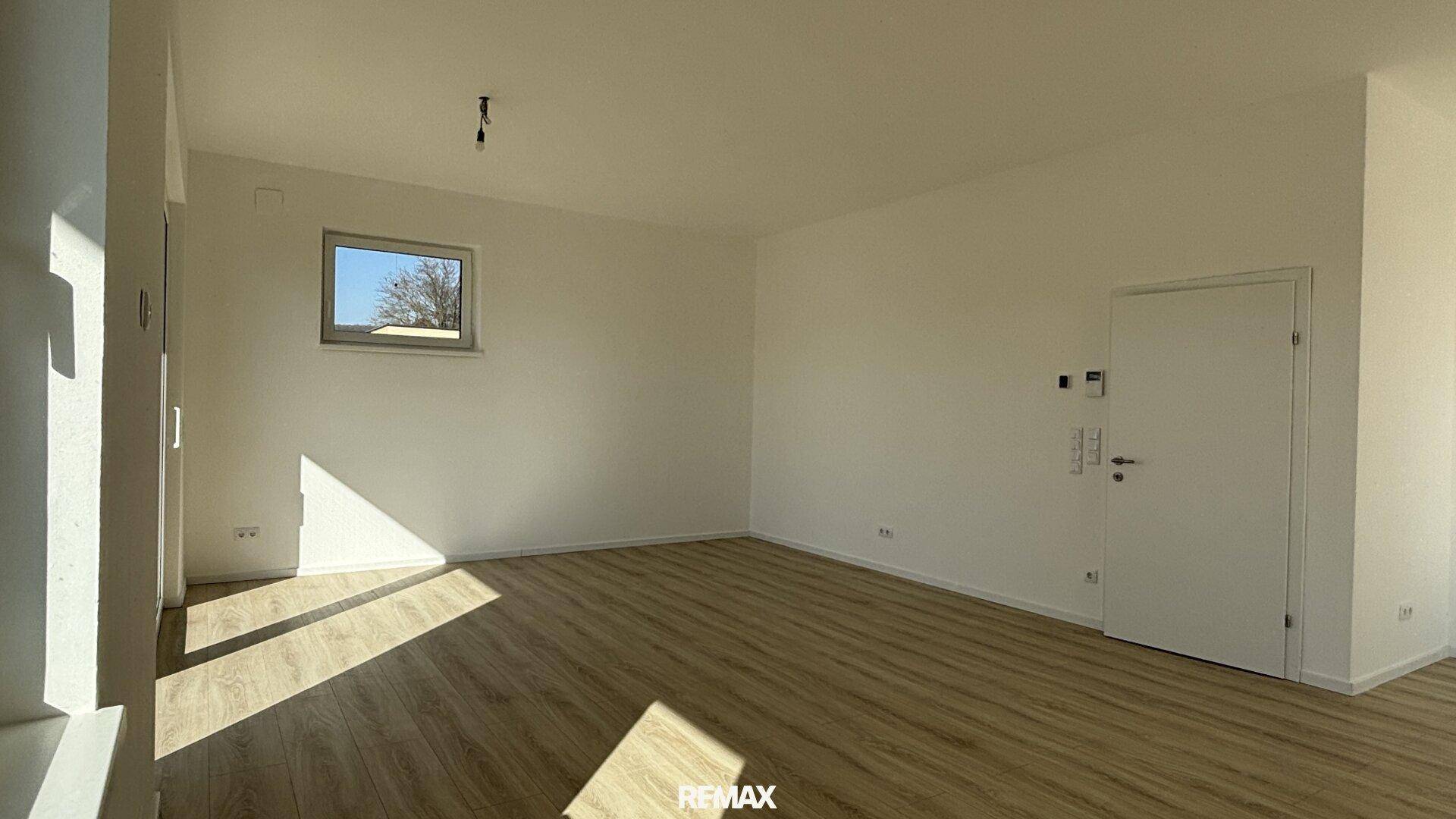 Lichtdurchfluteter Raum mit Laminatboden und einem Fenster, ideal als Wohn- oder Schlafzimmer.