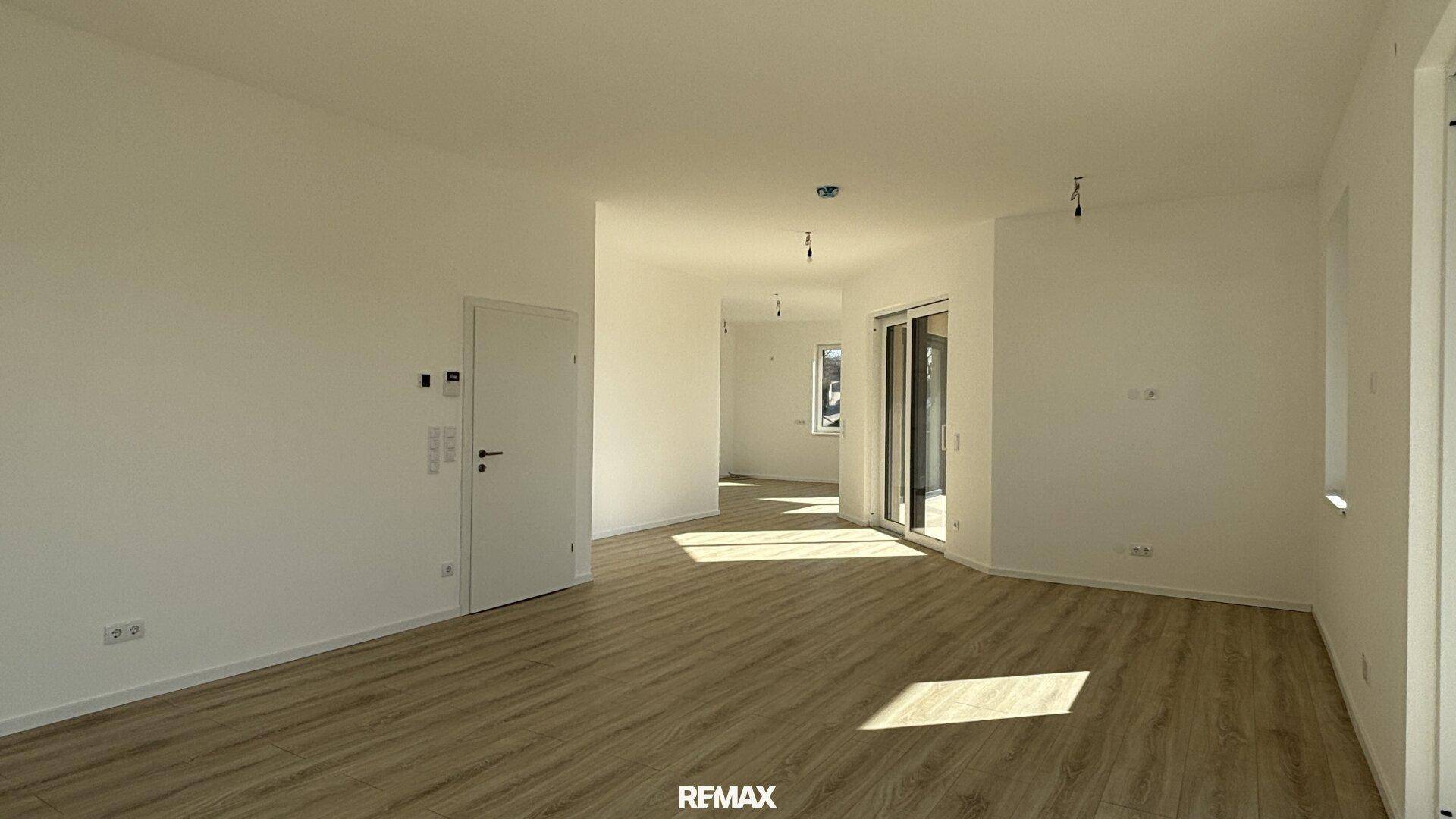 Großer, heller Wohnbereich mit Laminatboden und Zugang zu einem weiteren Raum und Terrasse.