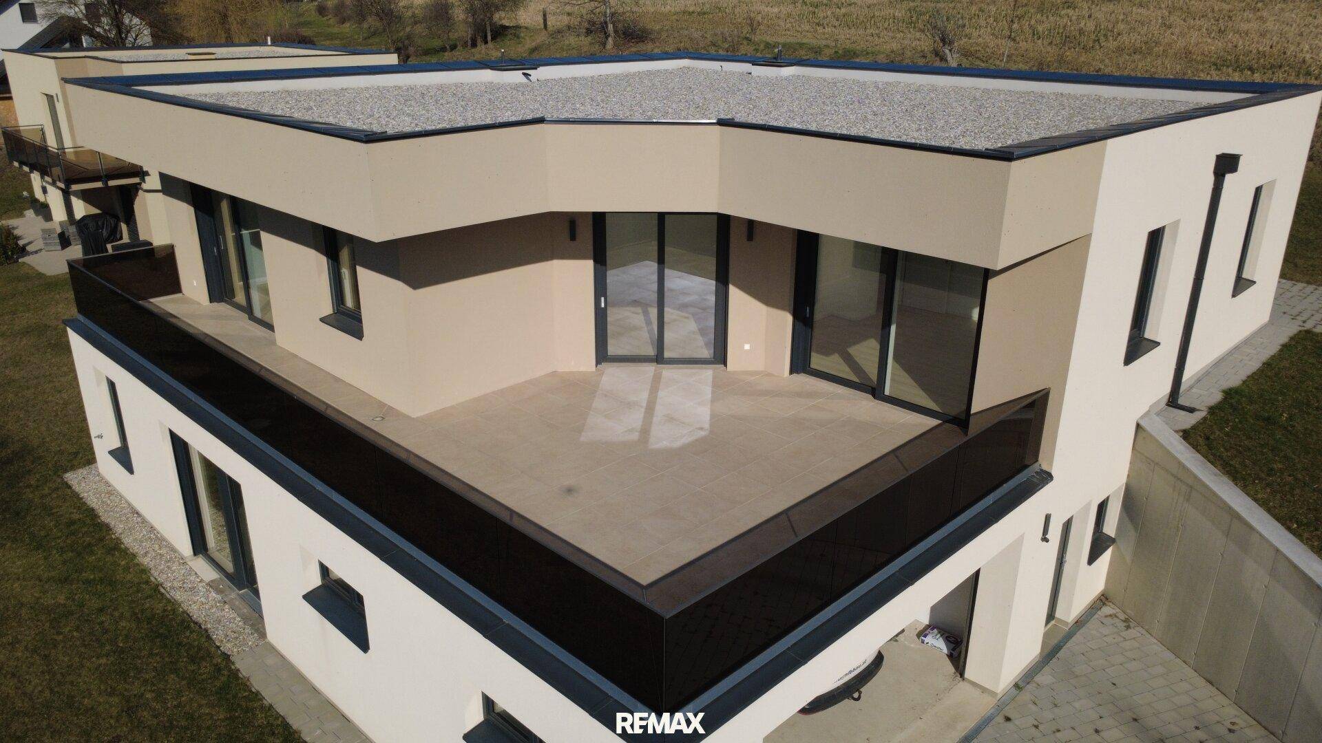 Große, moderne Terrasse mit Glasgeländer und Zugang zu den Innenräumen des Hauses.
