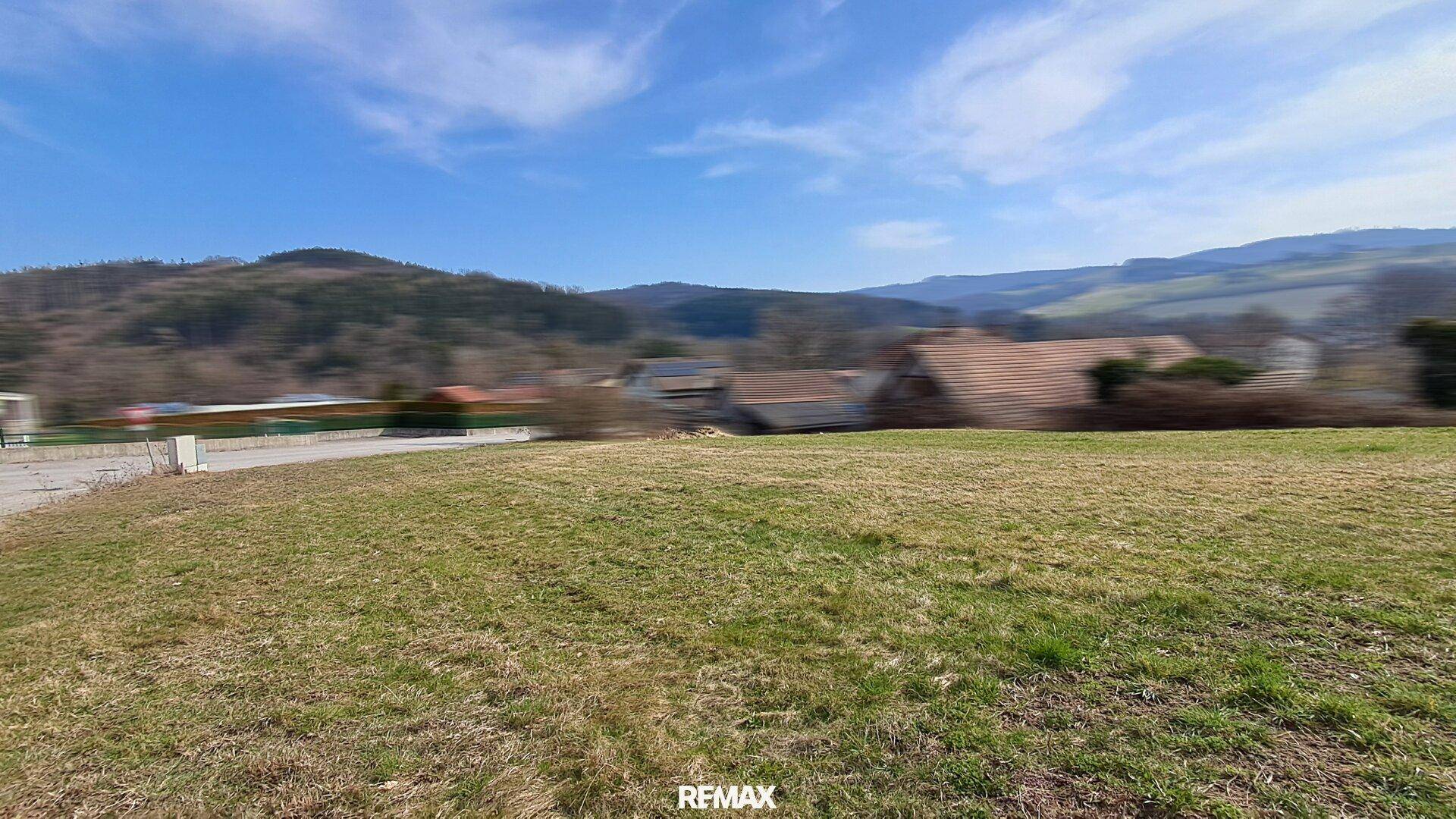 Blick vom Baugrundstück auf die umliegende Landschaft mit Hügeln und vereinzelten Häusern.