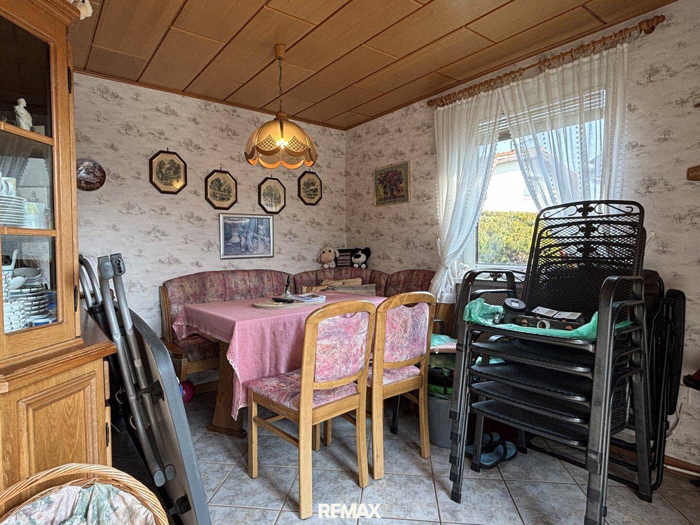 Gemütlicher Essbereich mit Holzdecke, floraler Tapete und Blick in den Garten.
