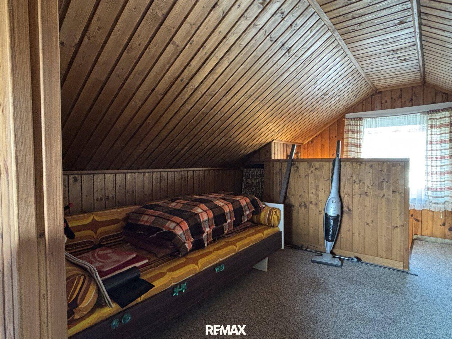 Gemütlicher Dachbodenraum mit Holzverkleidung, schrägen Wänden und kleinem Fenster.