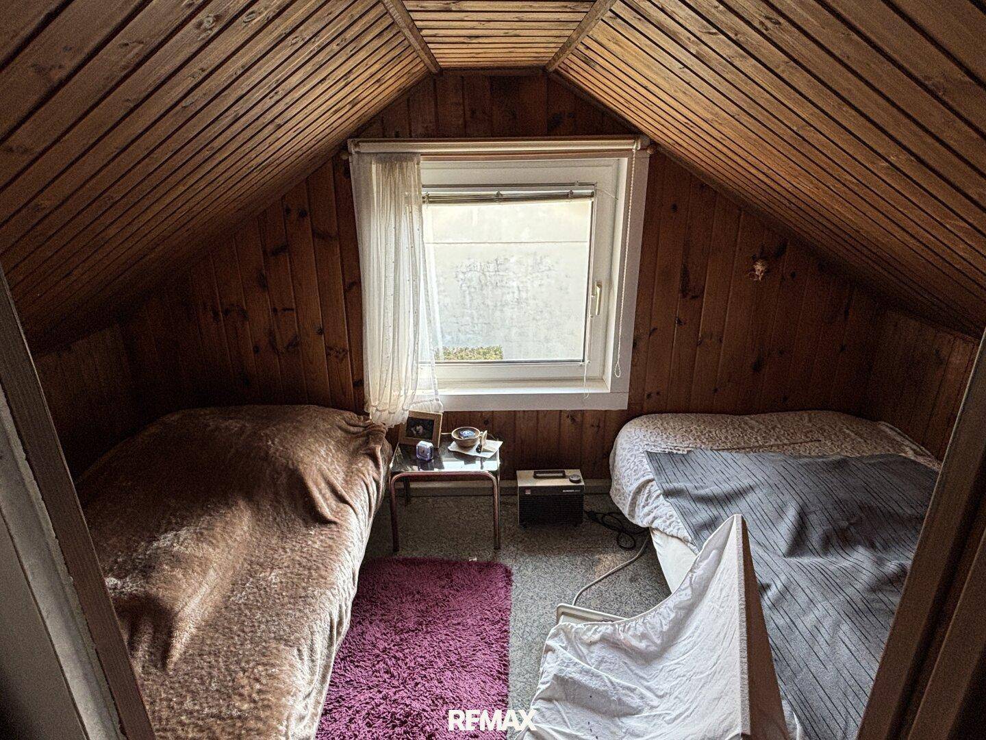 Dachboden-Schlafzimmer mit zwei Betten, Holzverkleidung und Fenster für Tageslicht.