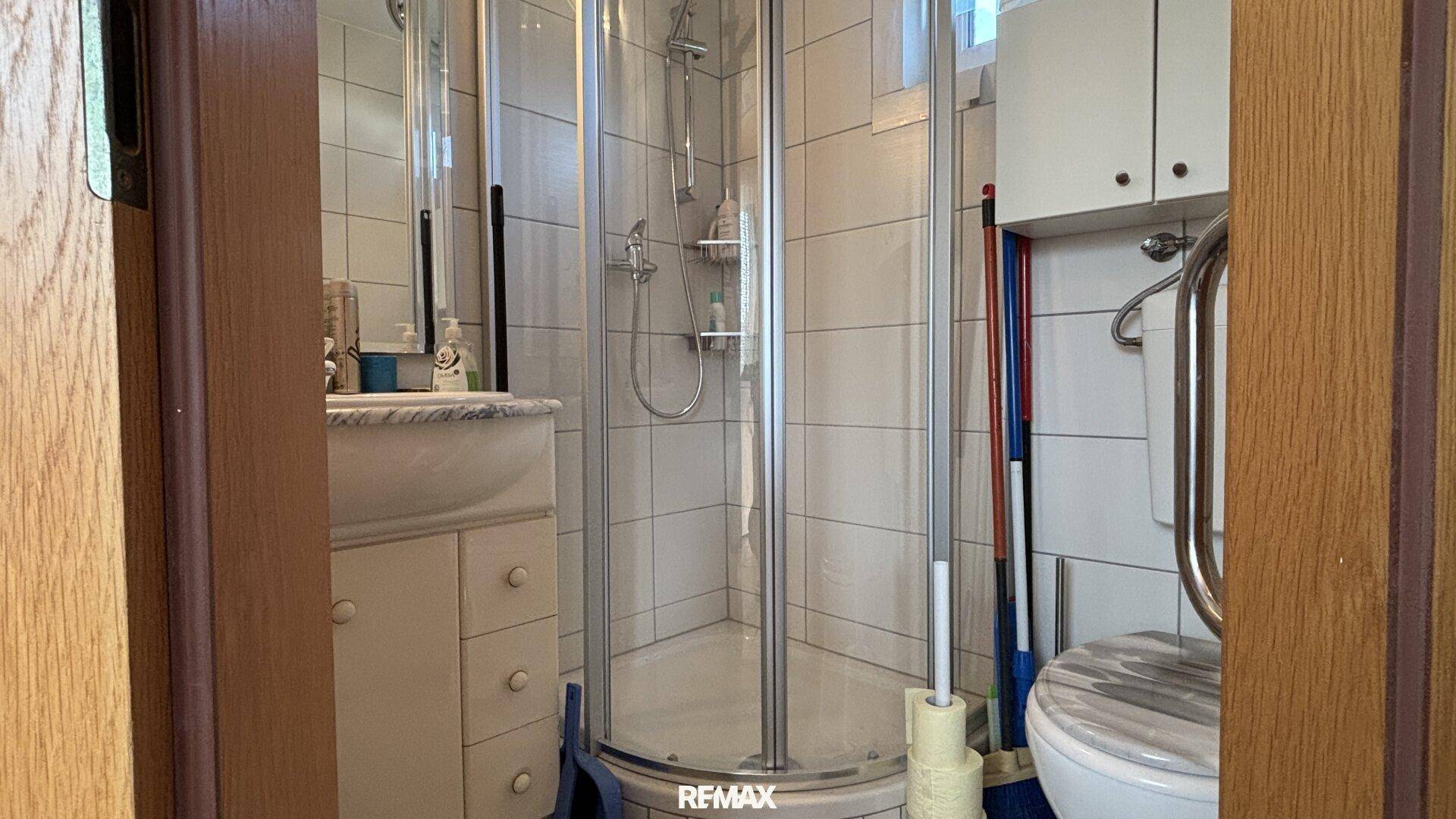 Badezimmer mit Eckdusche, Waschbecken, WC und praktischen Haltegriffen.