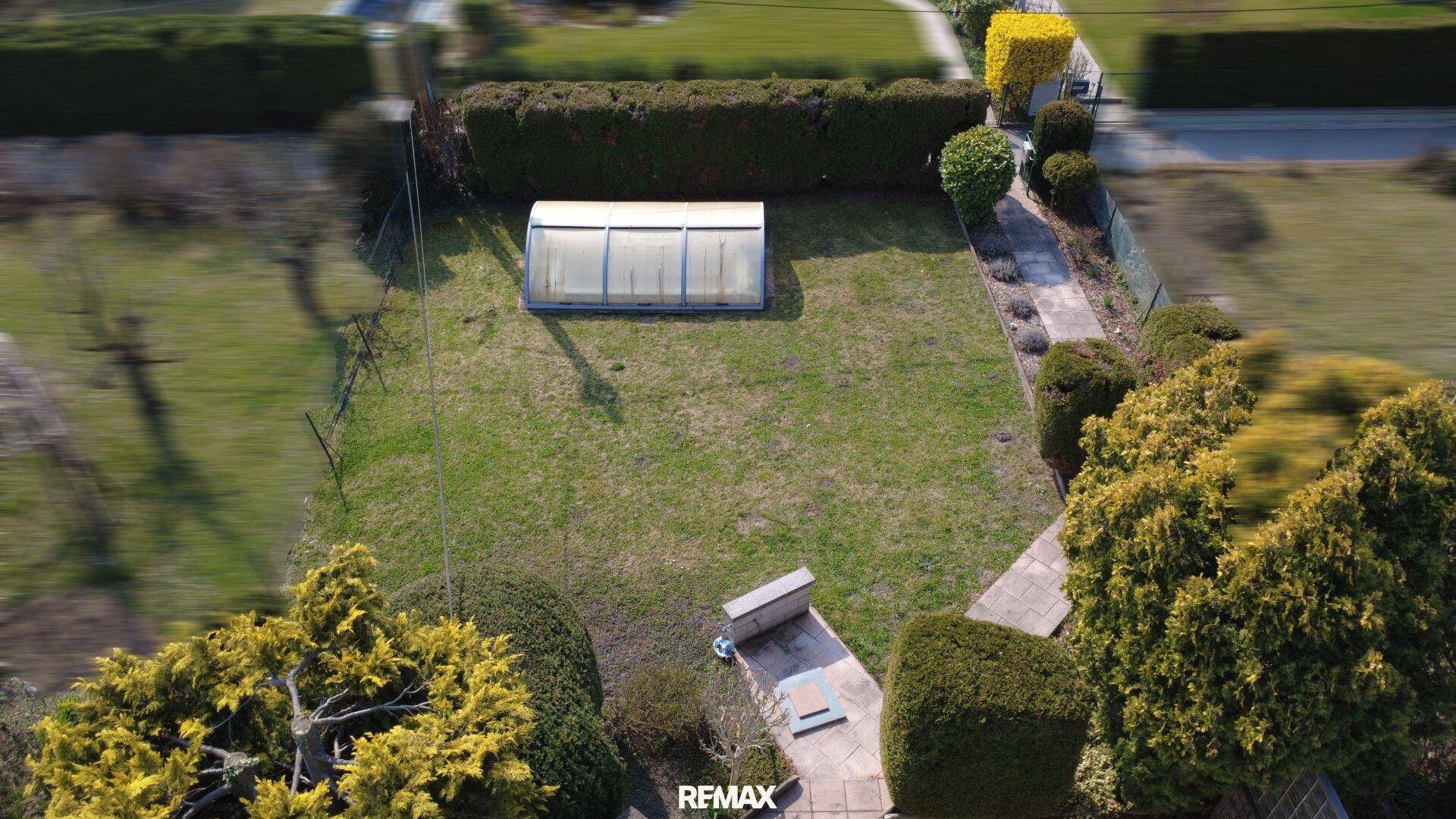 Großer, gepflegter Garten mit Rasenfläche und einem kleinen Gewächshaus.