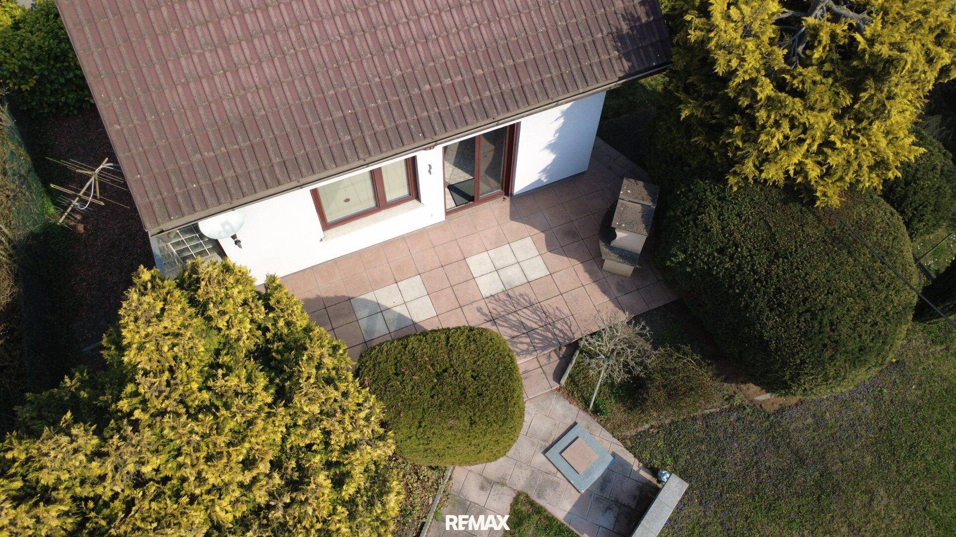 Geflieste Terrasse hinter dem Haus mit Grillplatz und Zugang zum Garten.