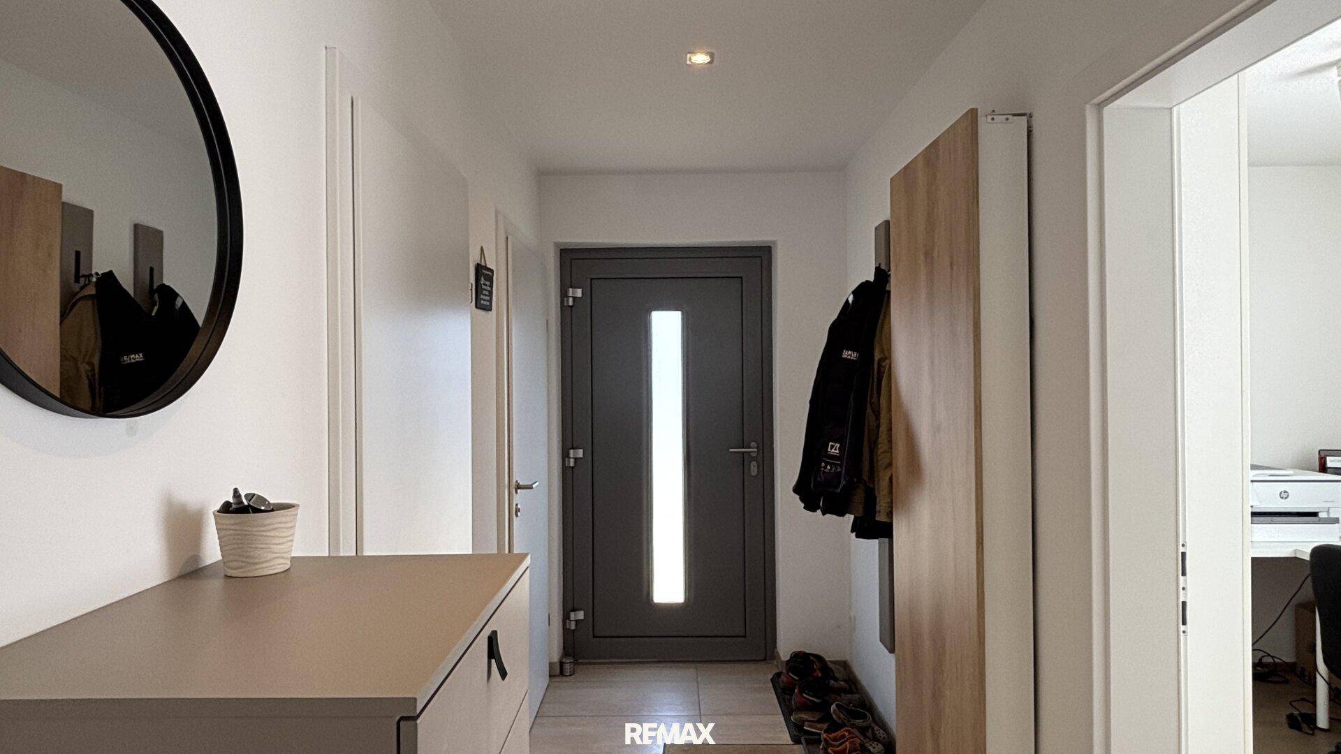 Heller Eingangsbereich mit moderner Haustür, Spiegel und Garderobe, ausgestattet mit Holzfußboden.