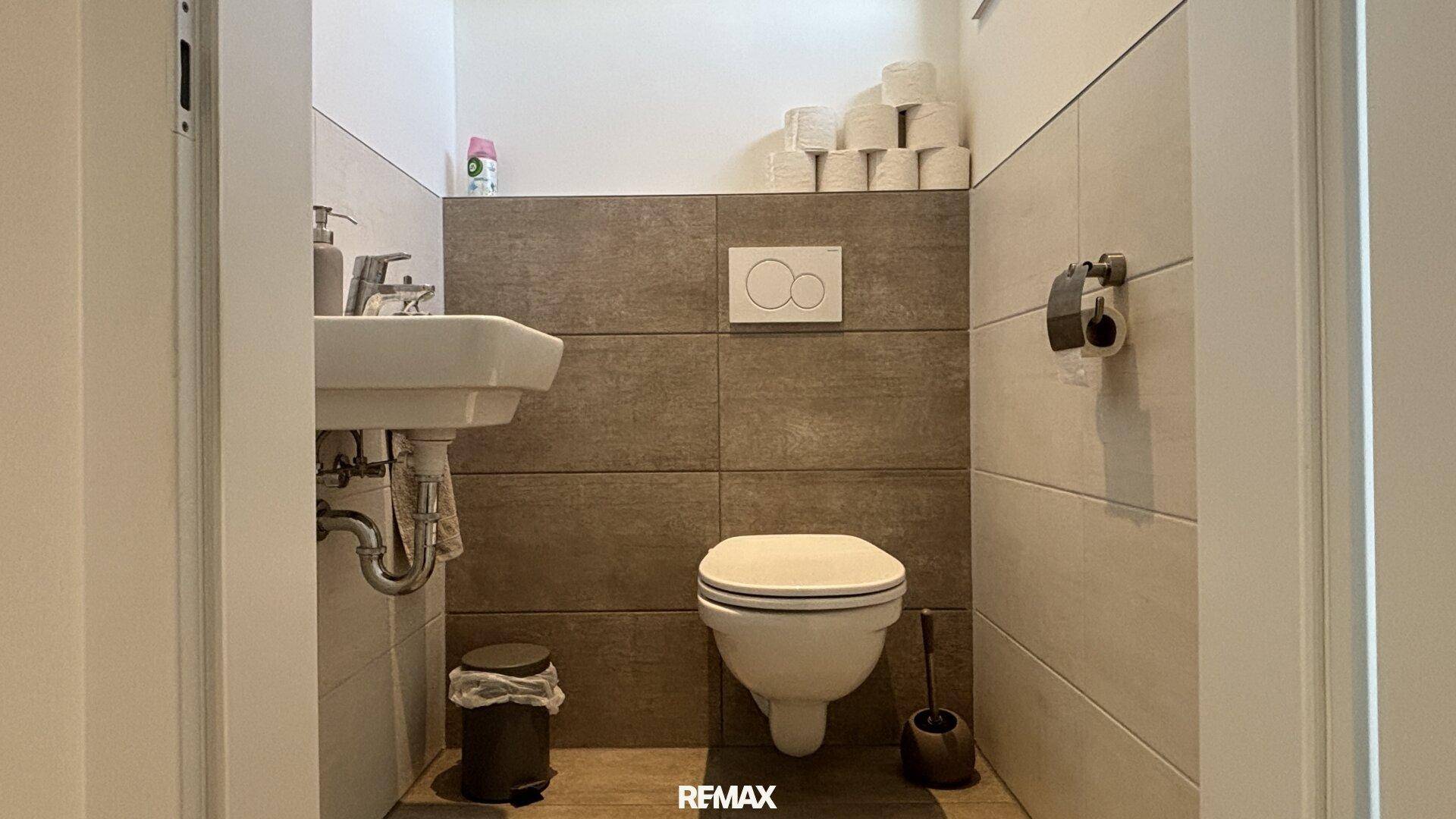 Kleines Gäste-WC mit wandhängendem WC und Waschbecken, halbhoch gefliest in neutralen Farben.