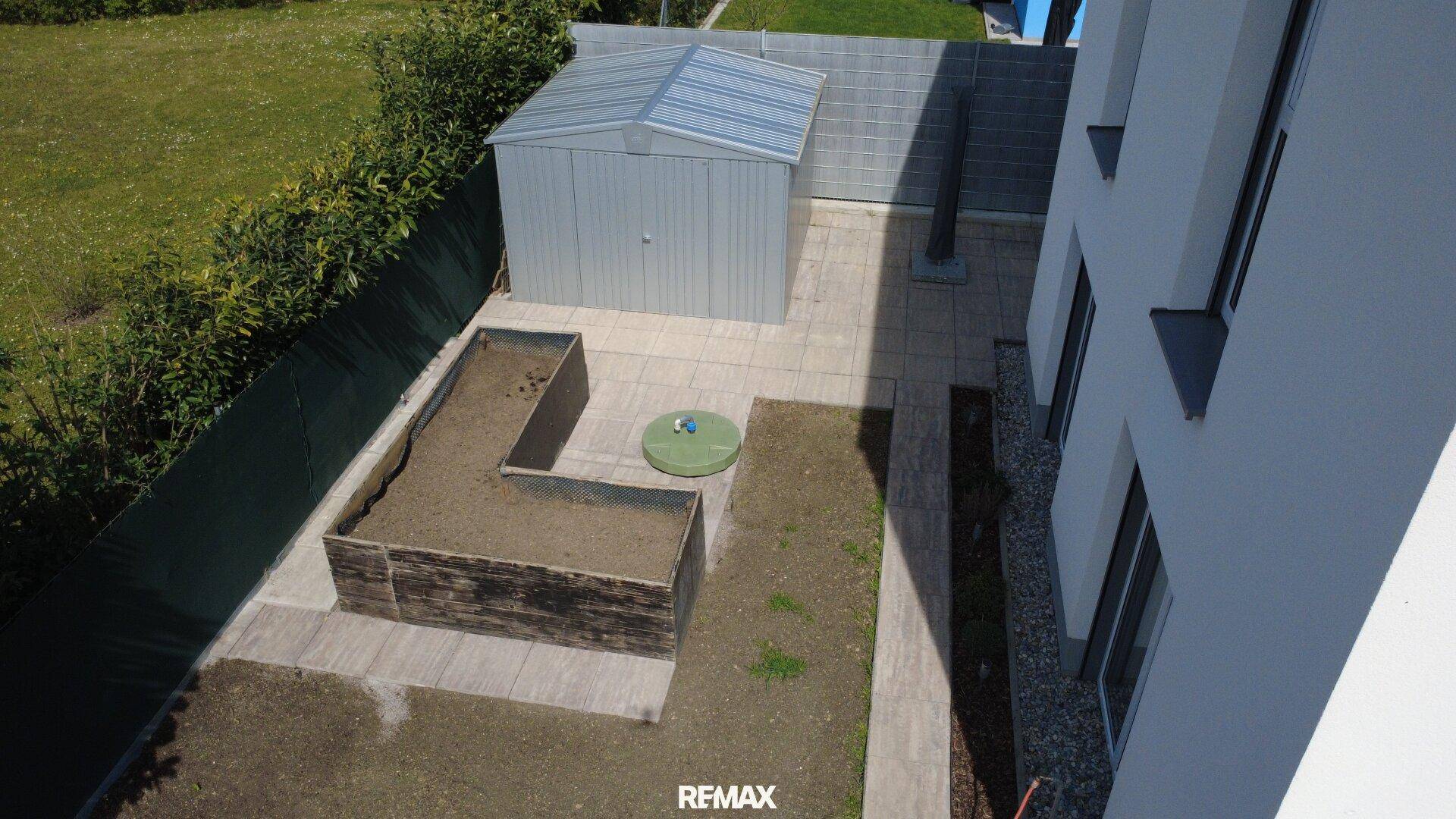 Draufsicht auf den Gartenbereich mit Gartenschuppen, Hochbeeten und gepflasterten Wegen.