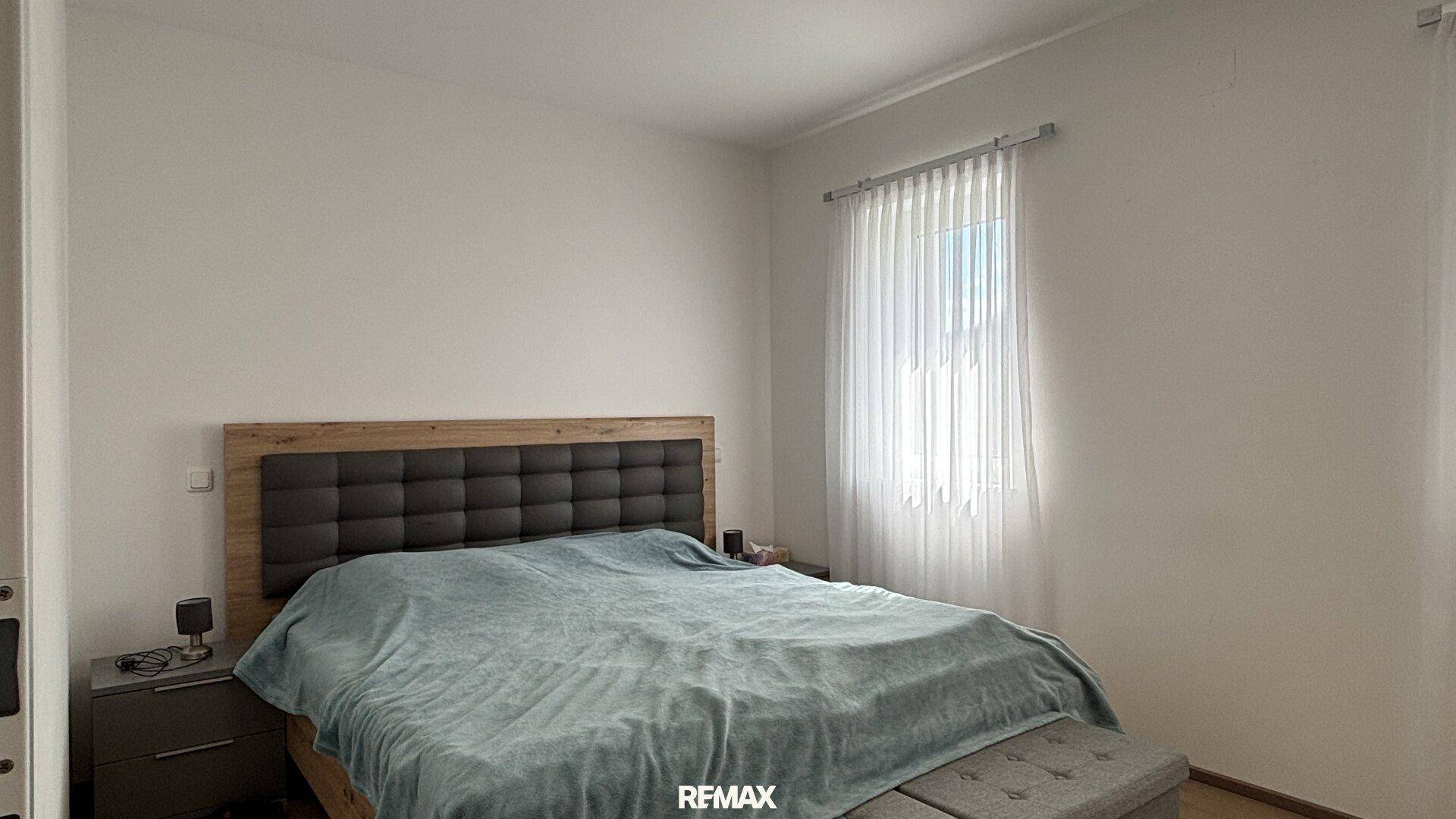 Gemütliches Schlafzimmer mit großem Doppelbett und gepolstertem Kopfteil, hell durch Fenster.