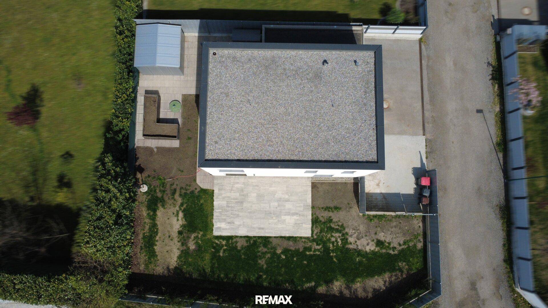 Direkte Draufsicht auf das Flachdach des Hauses und die umliegende Grundstücksgestaltung.