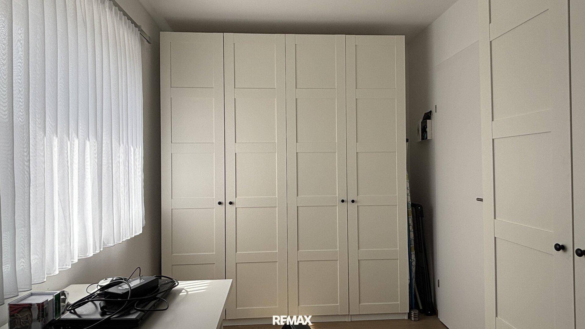 Schlafzimmer mit großen, weißen Einbauschränken und viel Stauraum, hell durch Fenster.
