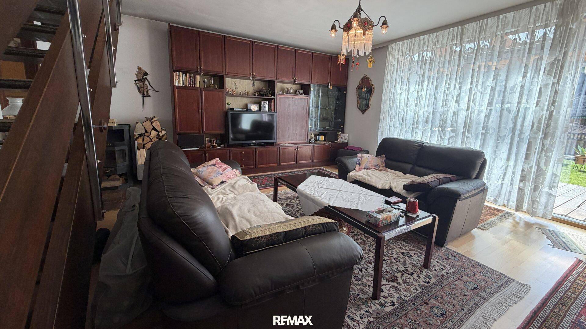 Gemütliches Wohnzimmer mit dunklen Ledersofas, Holzmöbeln und Zugang zum Garten.