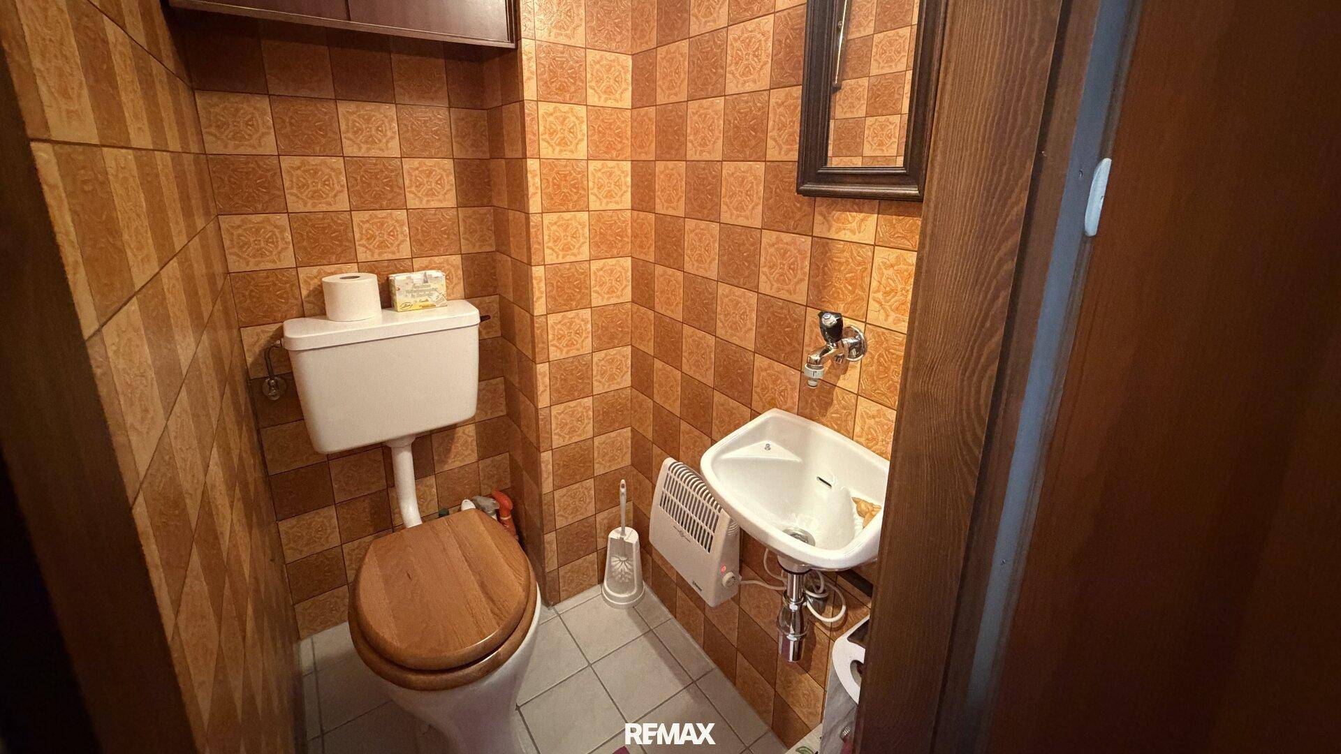 Kleines Gäste-WC mit braunen Fliesen, WC und Waschbecken.