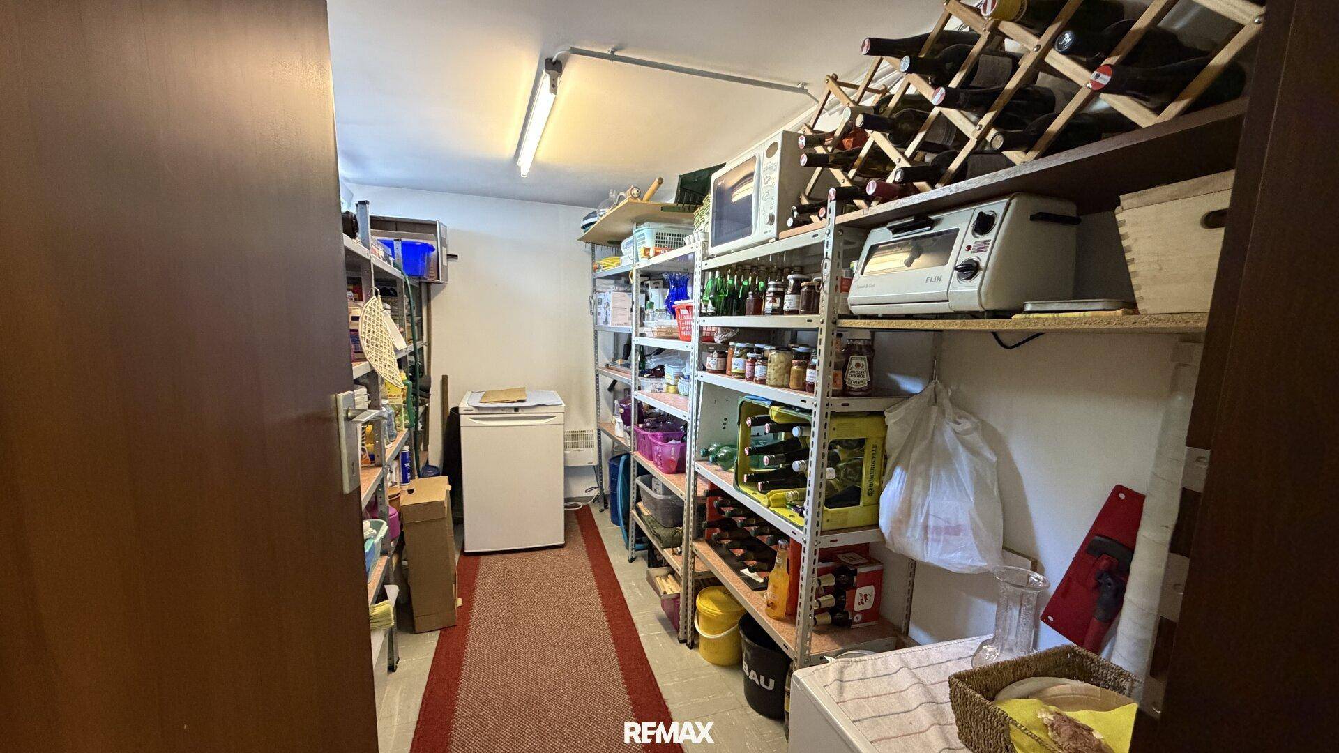 Geräumiger Vorratsraum mit Regalen, Weinflaschen und einem Kühlschrank.