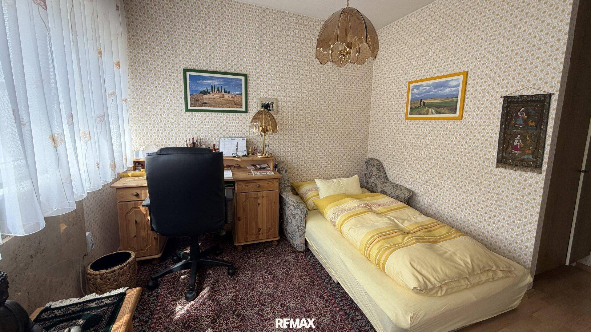 Helles Schlafzimmer mit Einzelbett, Schreibtisch und Teppichboden.