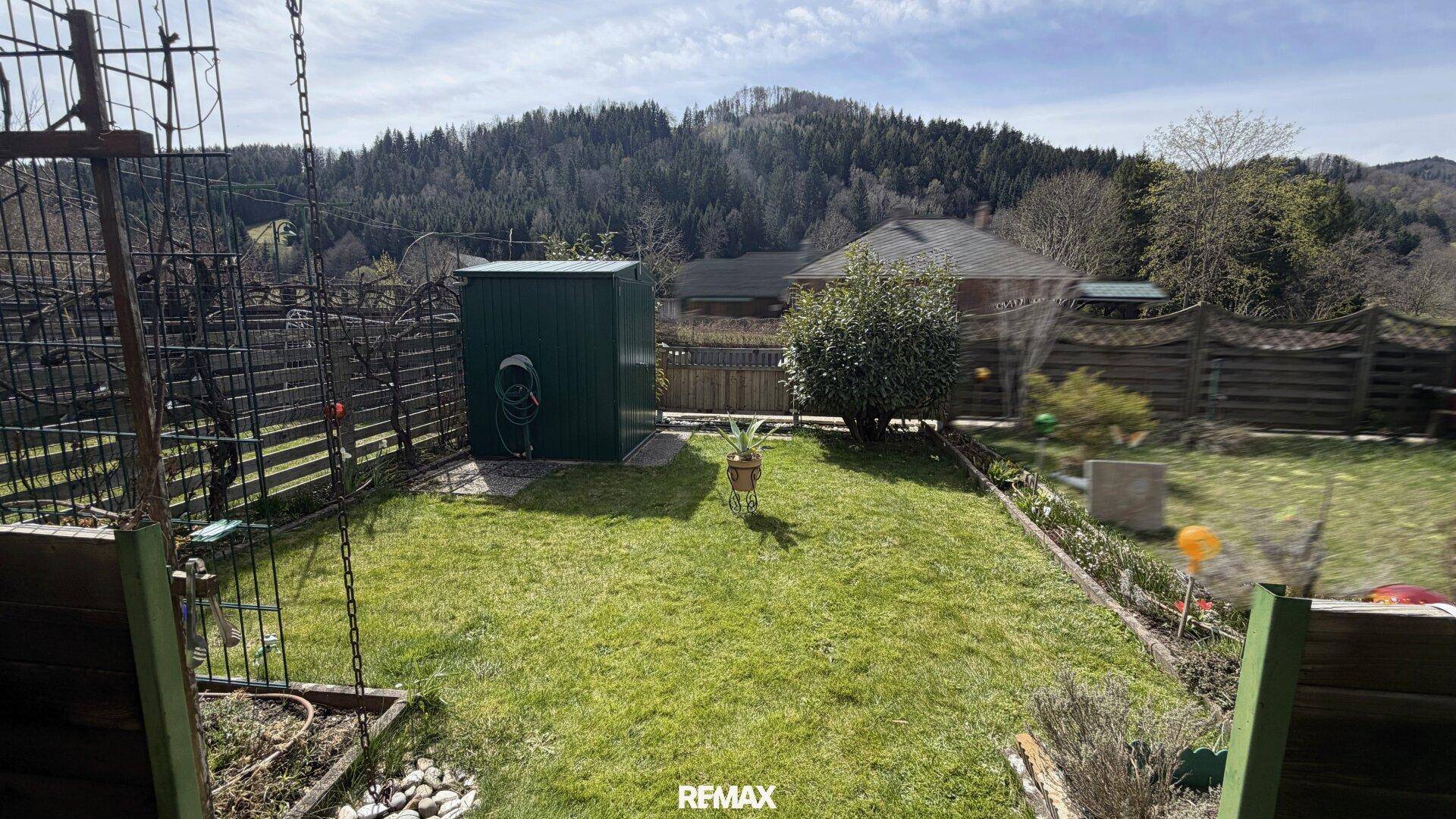 Gepflegter Garten mit Rasenfläche, Gartenhaus und Bergblick.