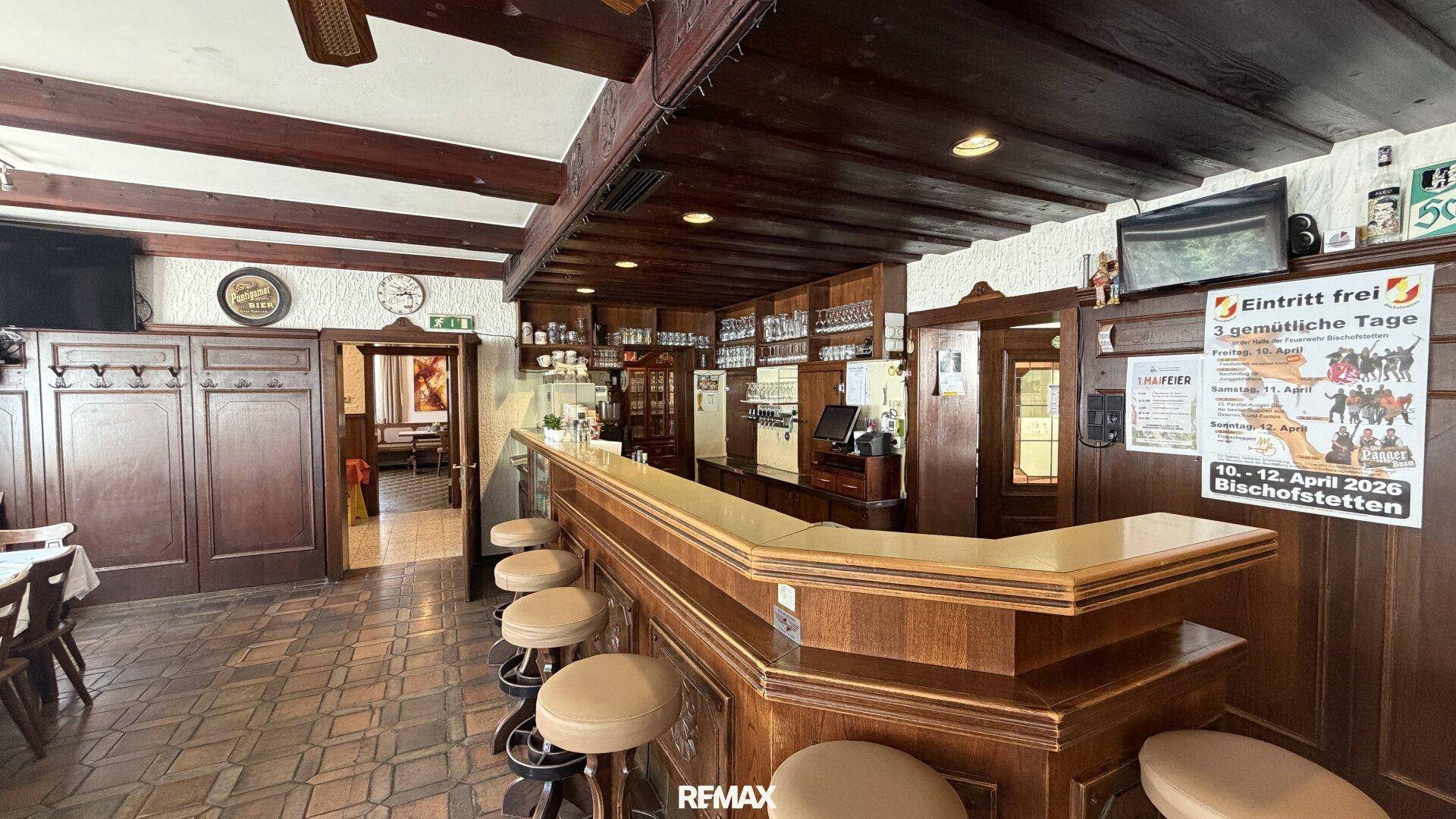 Rustikale Bar mit Holzelementen, Hockern und traditionellem Fliesenboden in einem Gasthaus.